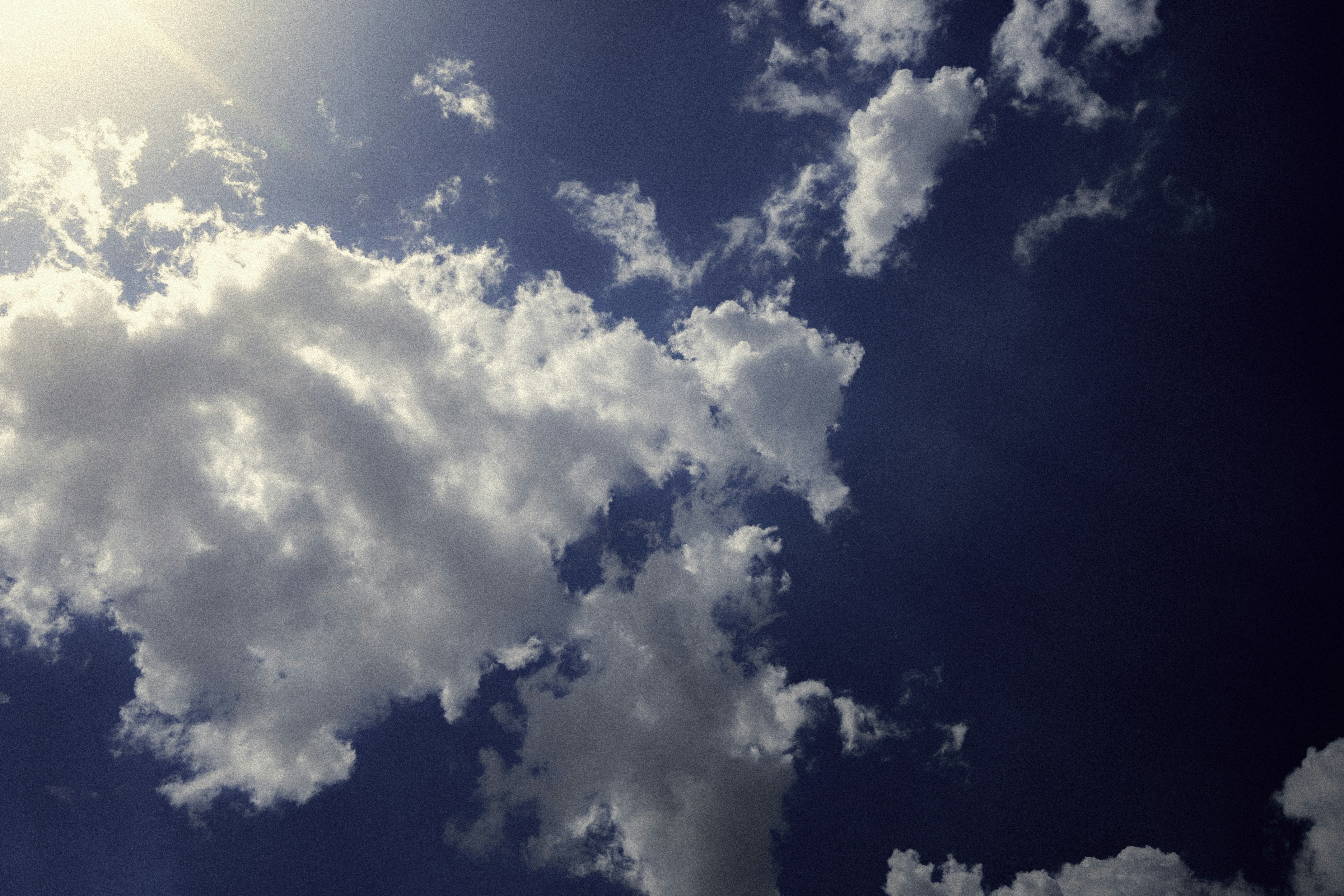 Un soleil éclatant traverse les nuages blancs et duveteux dans un ciel bleu.