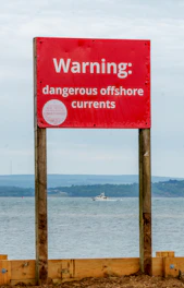 Red warning sign for dangerous offshore currents near a boat
