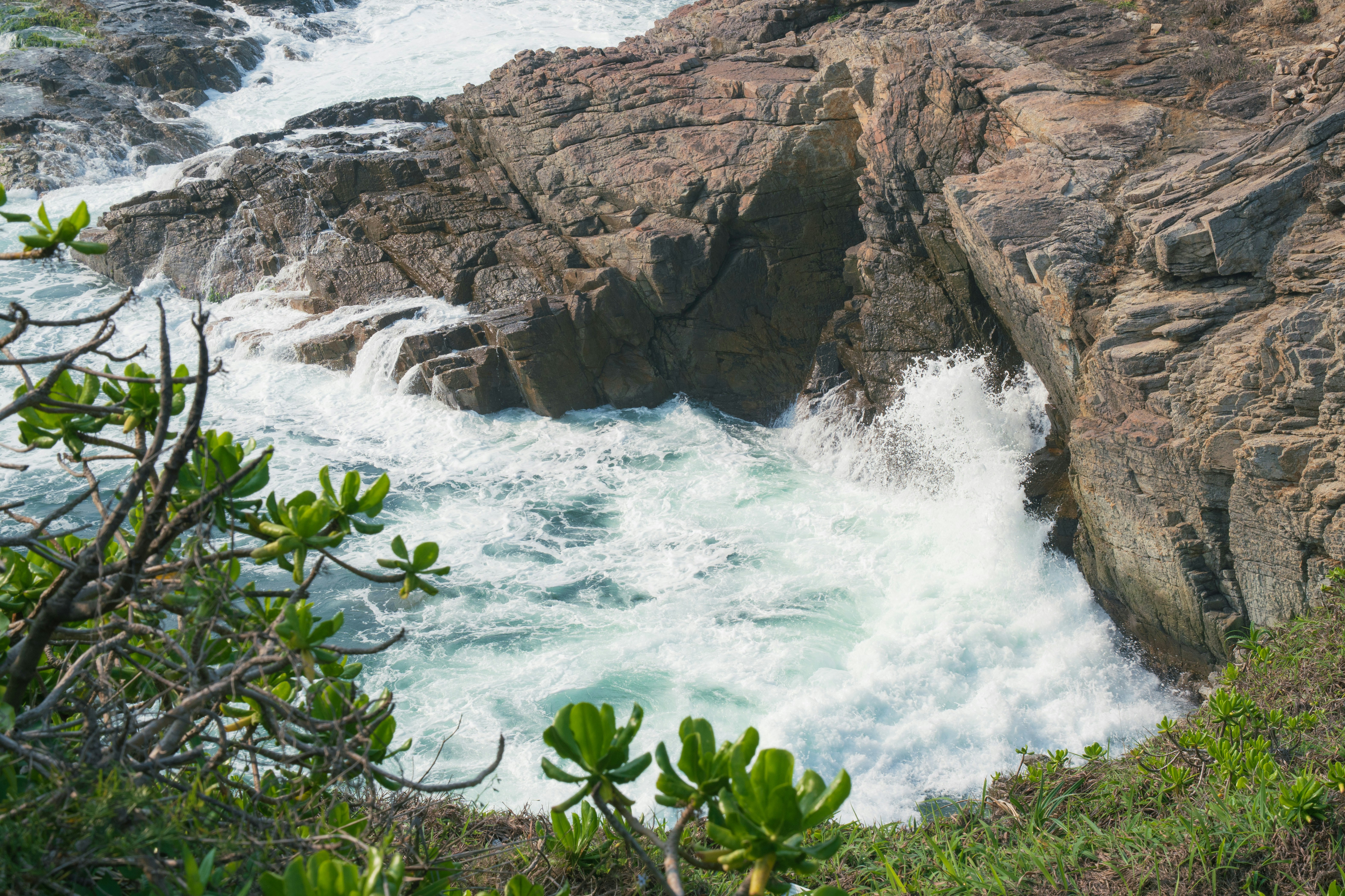 Waves crash against rocky cliffs with green foliage.