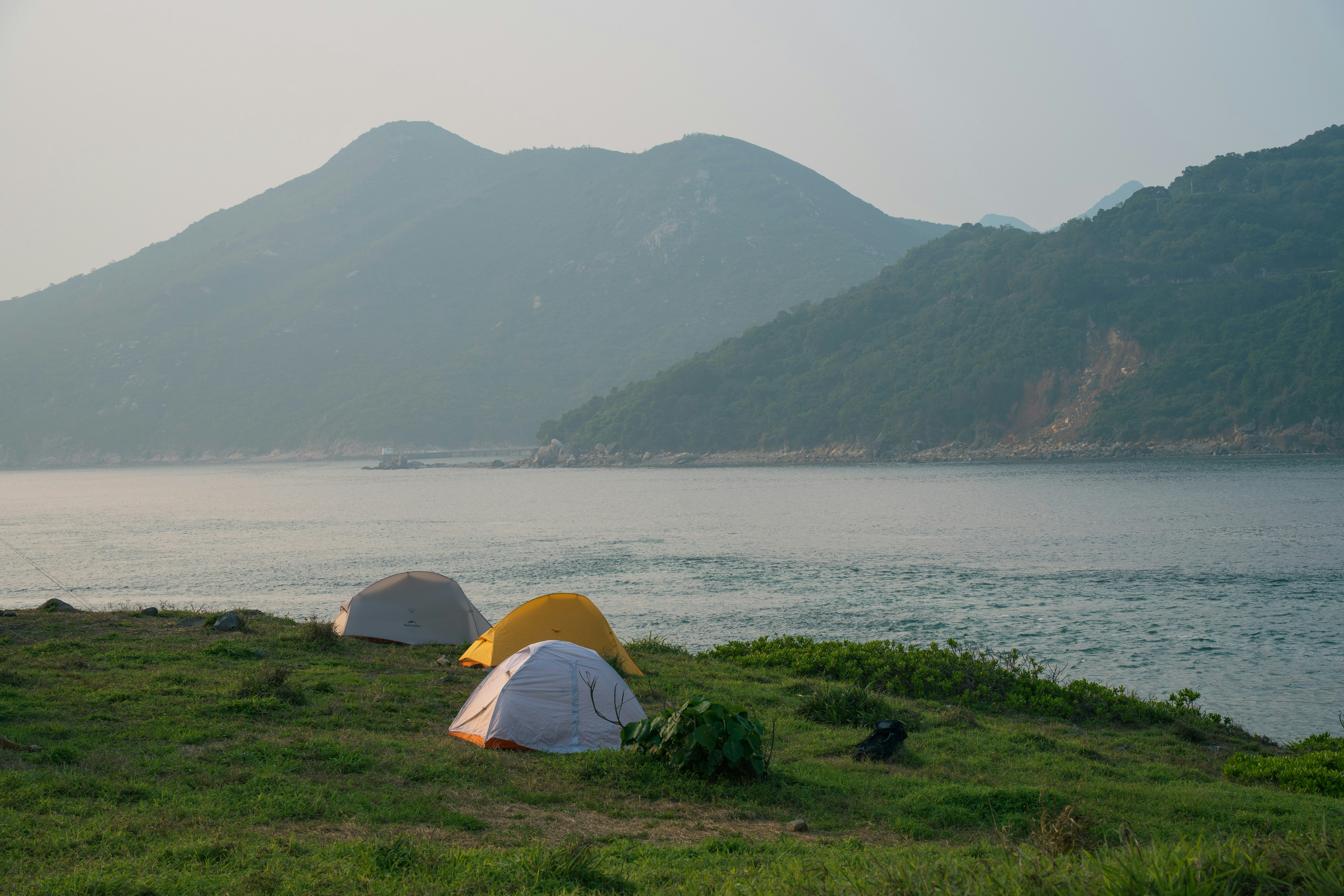 Camping tents on a coastal hill with mountains and sea.