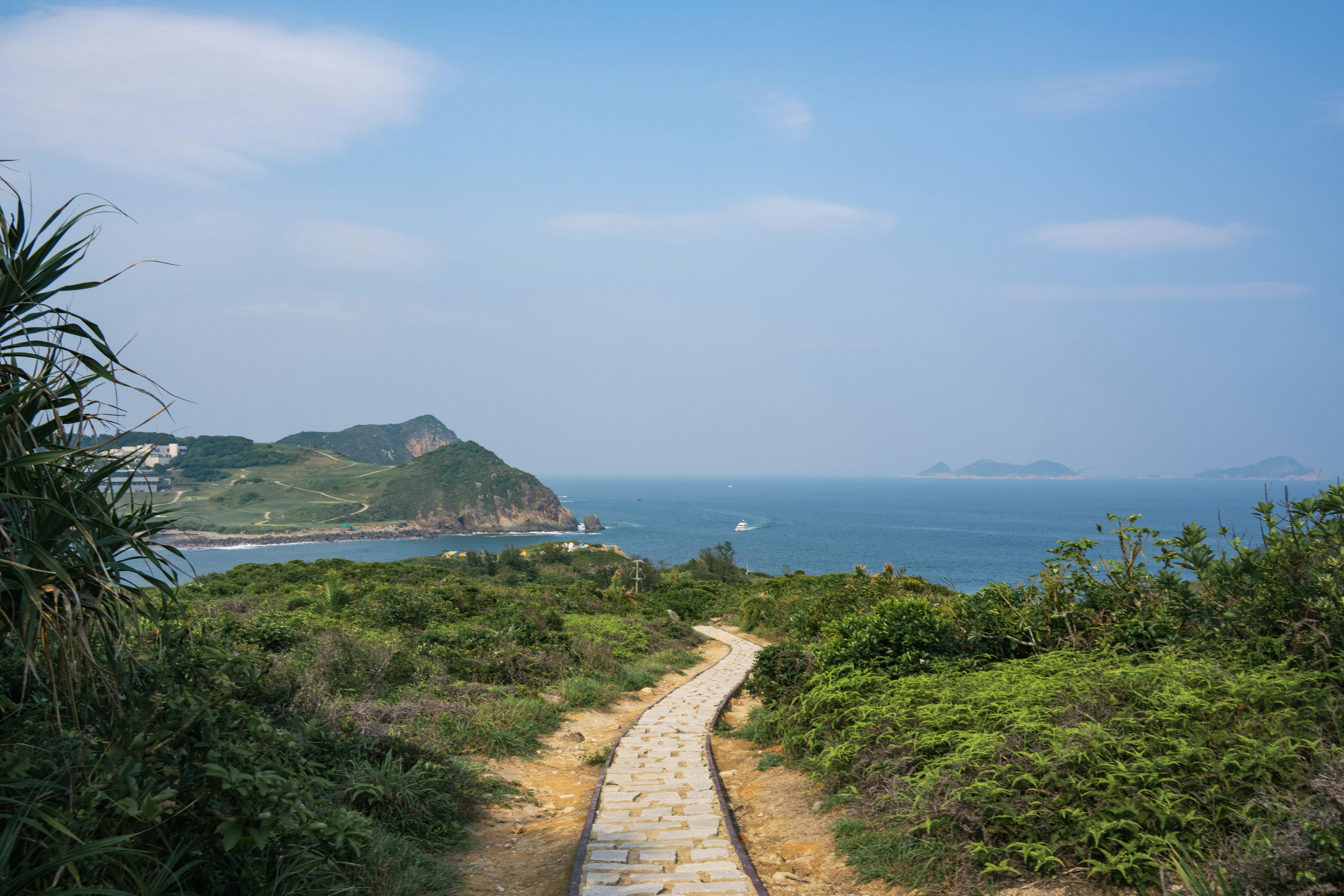 A stone path leads to the ocean with green hills.