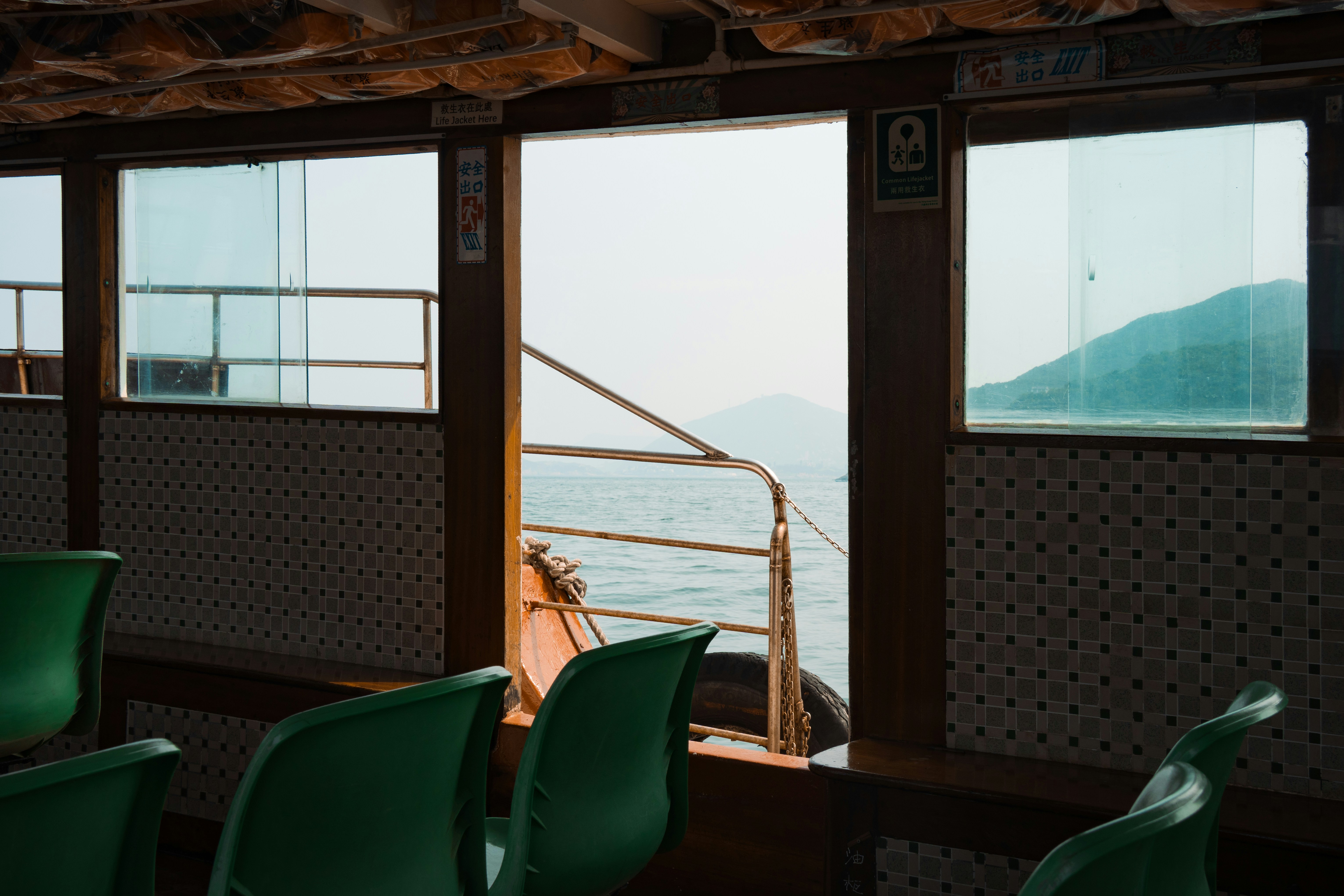 Boat interior with green seats, ocean, and distant mountains.