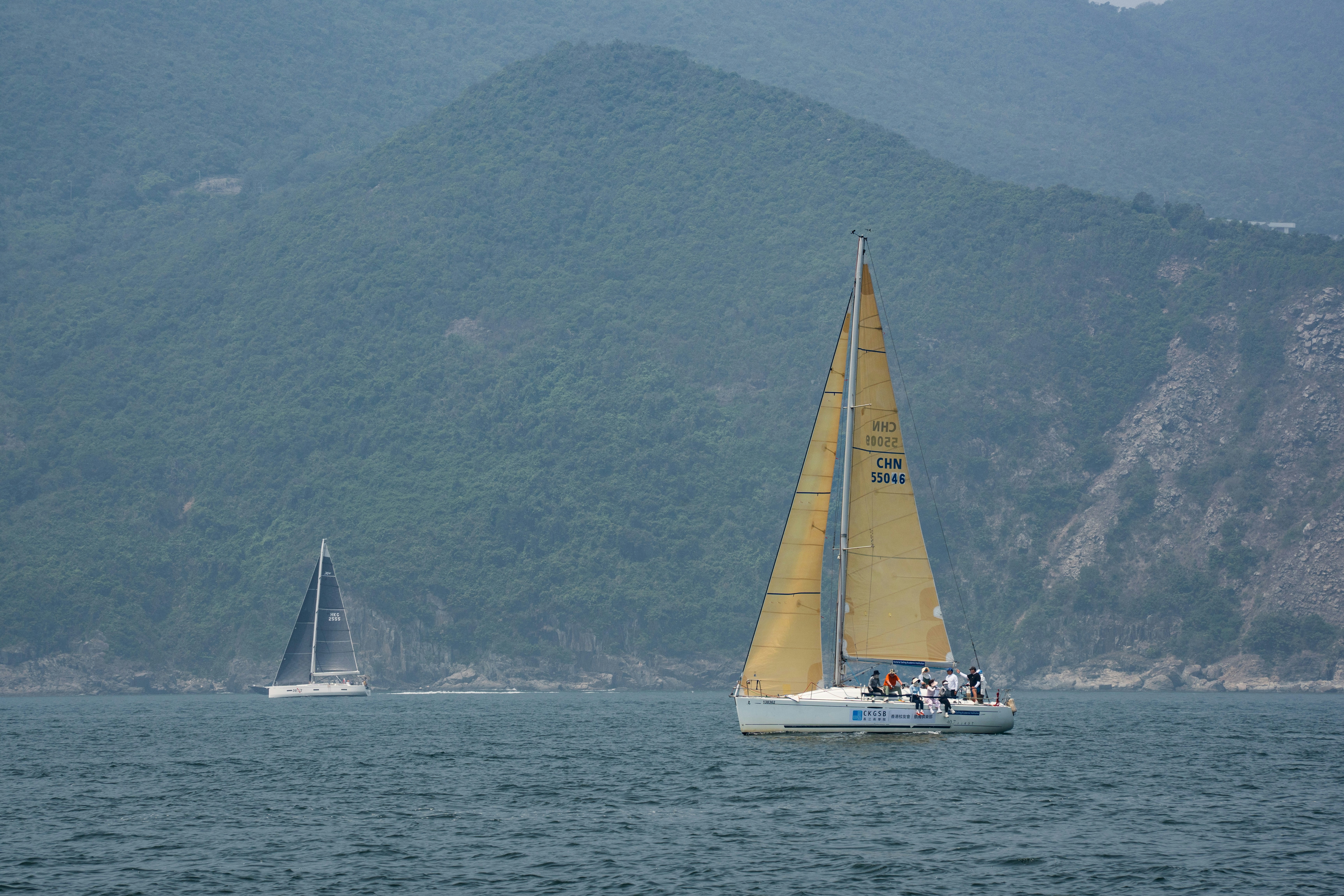 Two sailboats on the sea with green mountains in background.