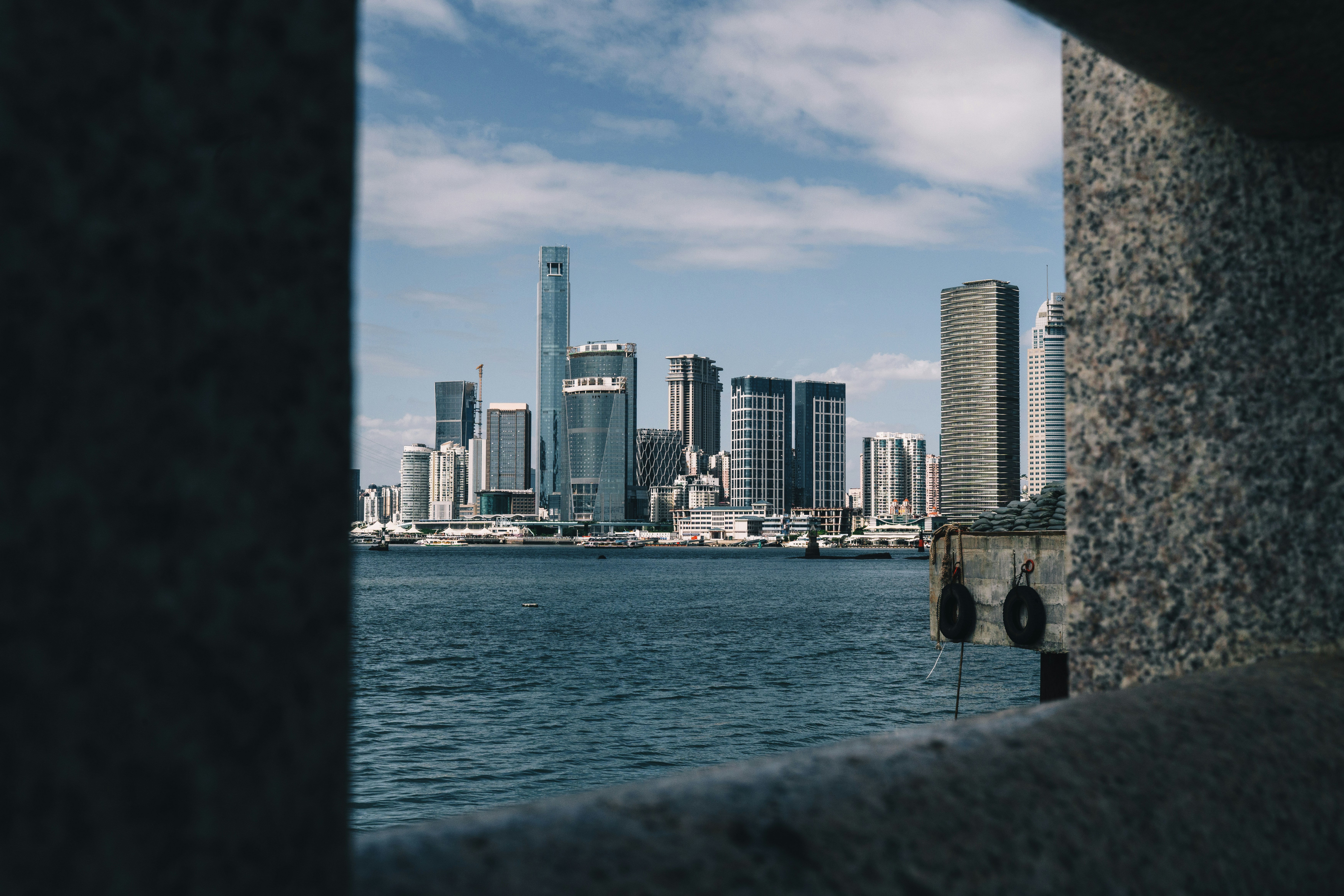 Urban skyline with skyscrapers over water, framed by stone.