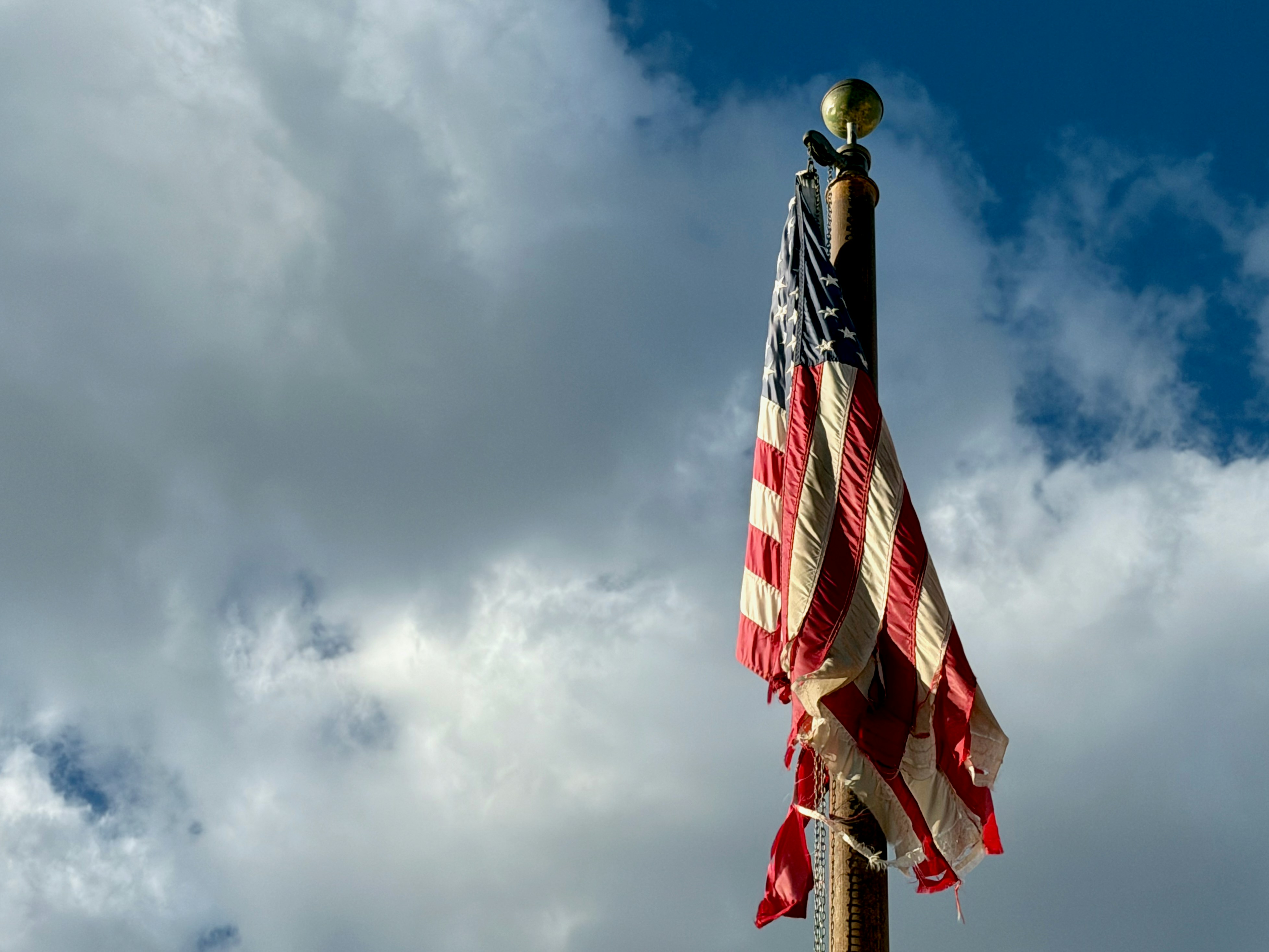Tattered american flag waves against a cloudy sky