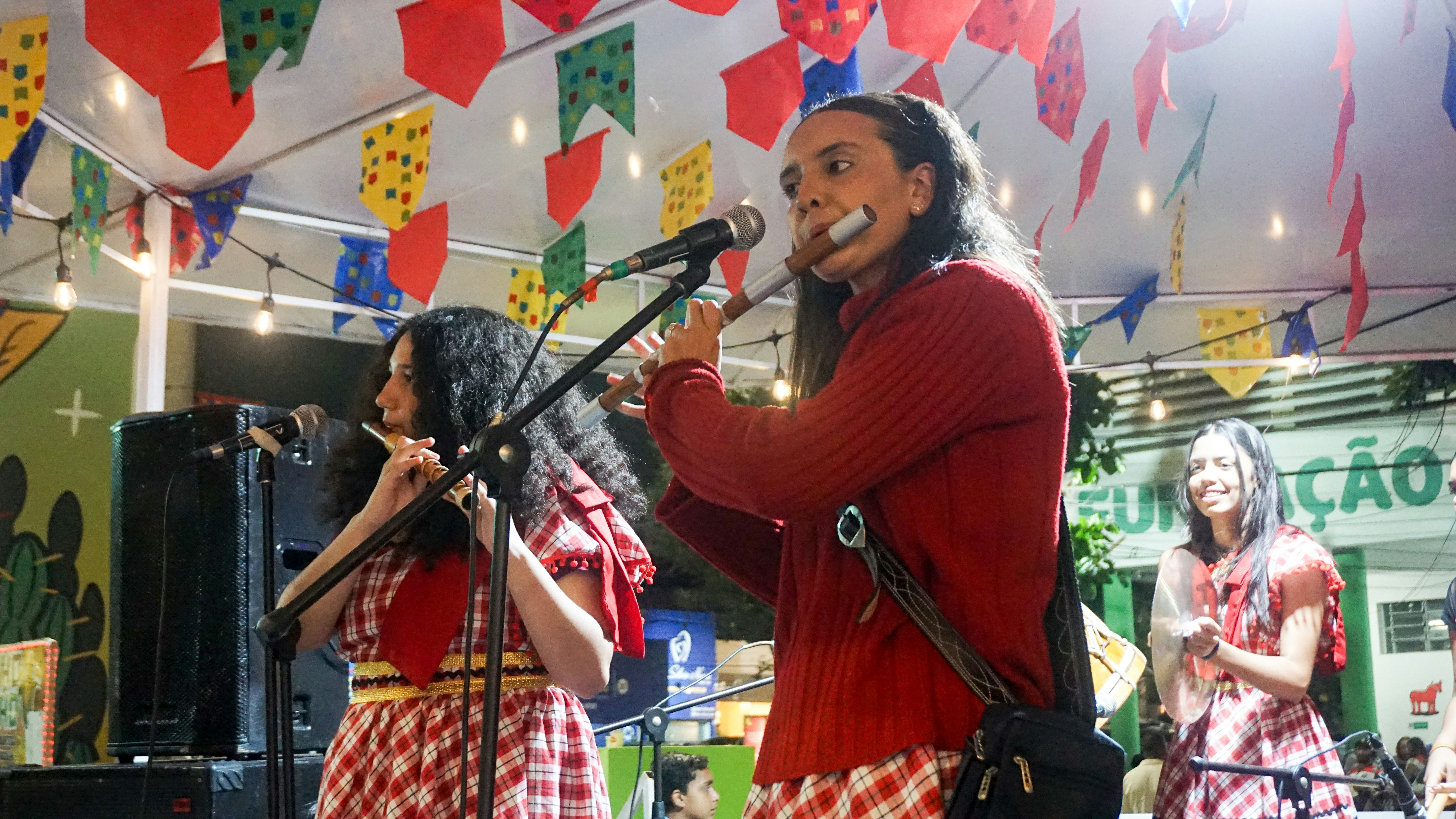 Two women play flutes on stage with festive decorations.