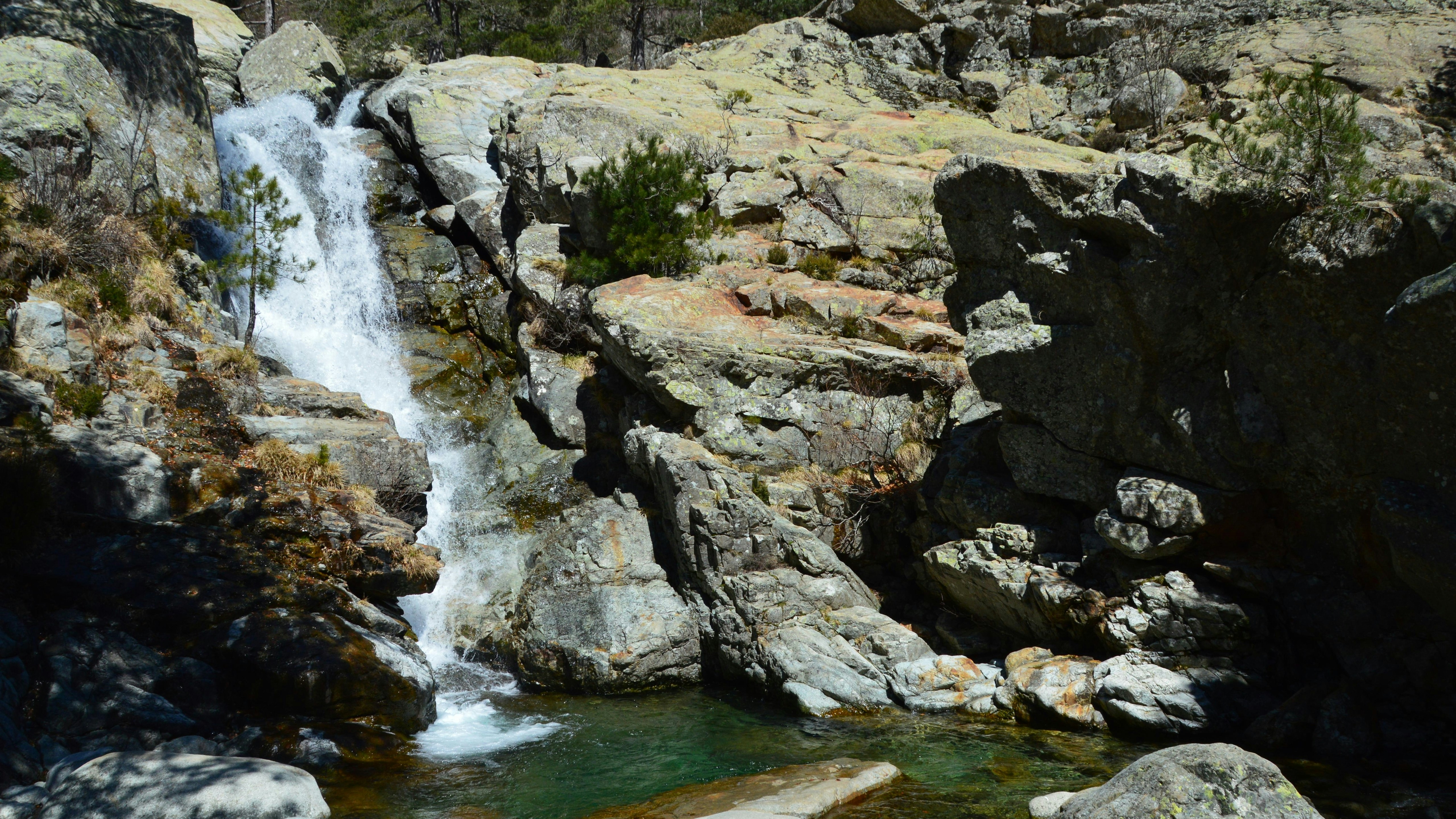Una cascata scende su un terreno roccioso fino a una piscina limpida.