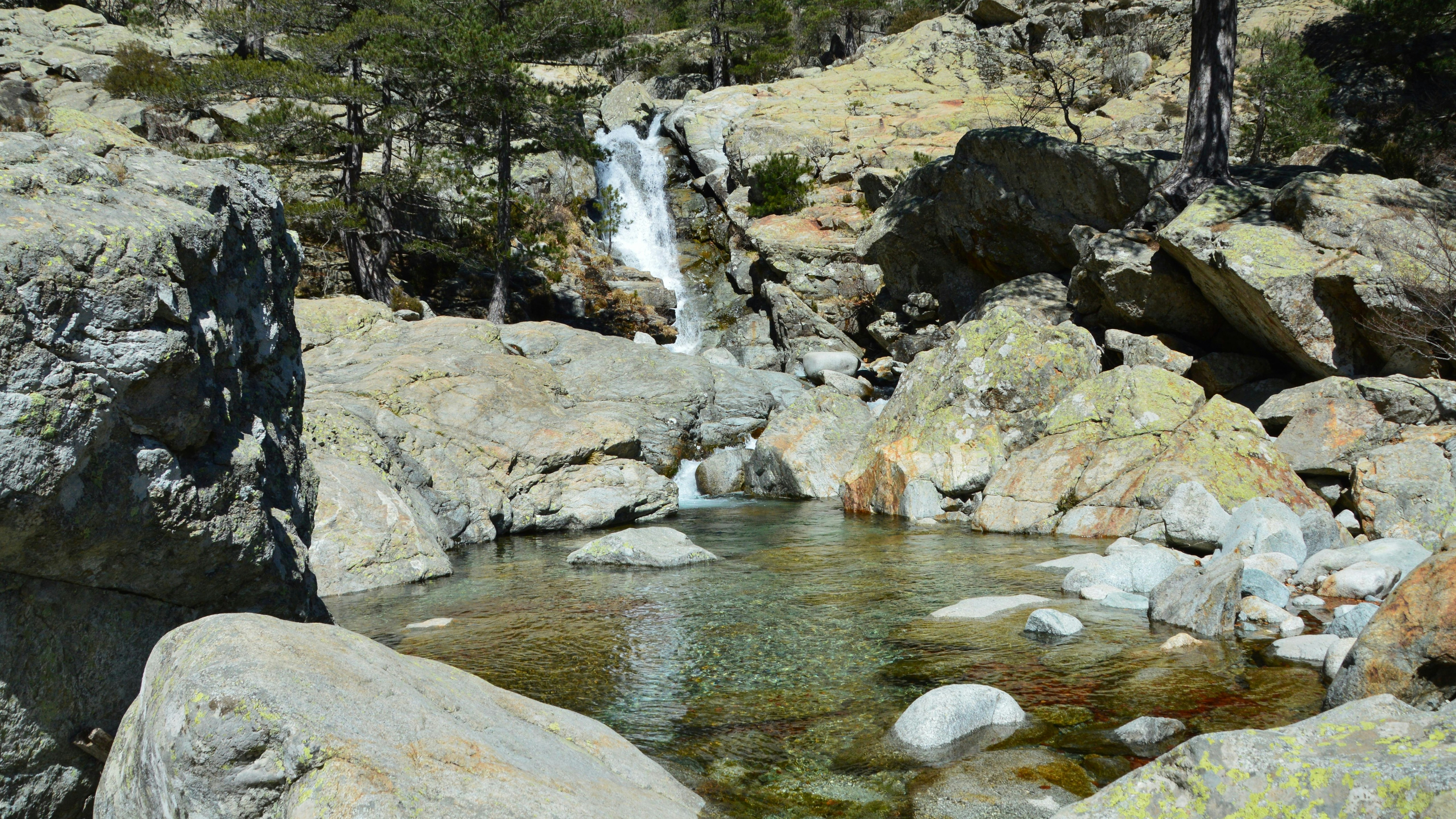 Paesaggio di montagne rocciose con una cascata che scende e una piscina limpida.