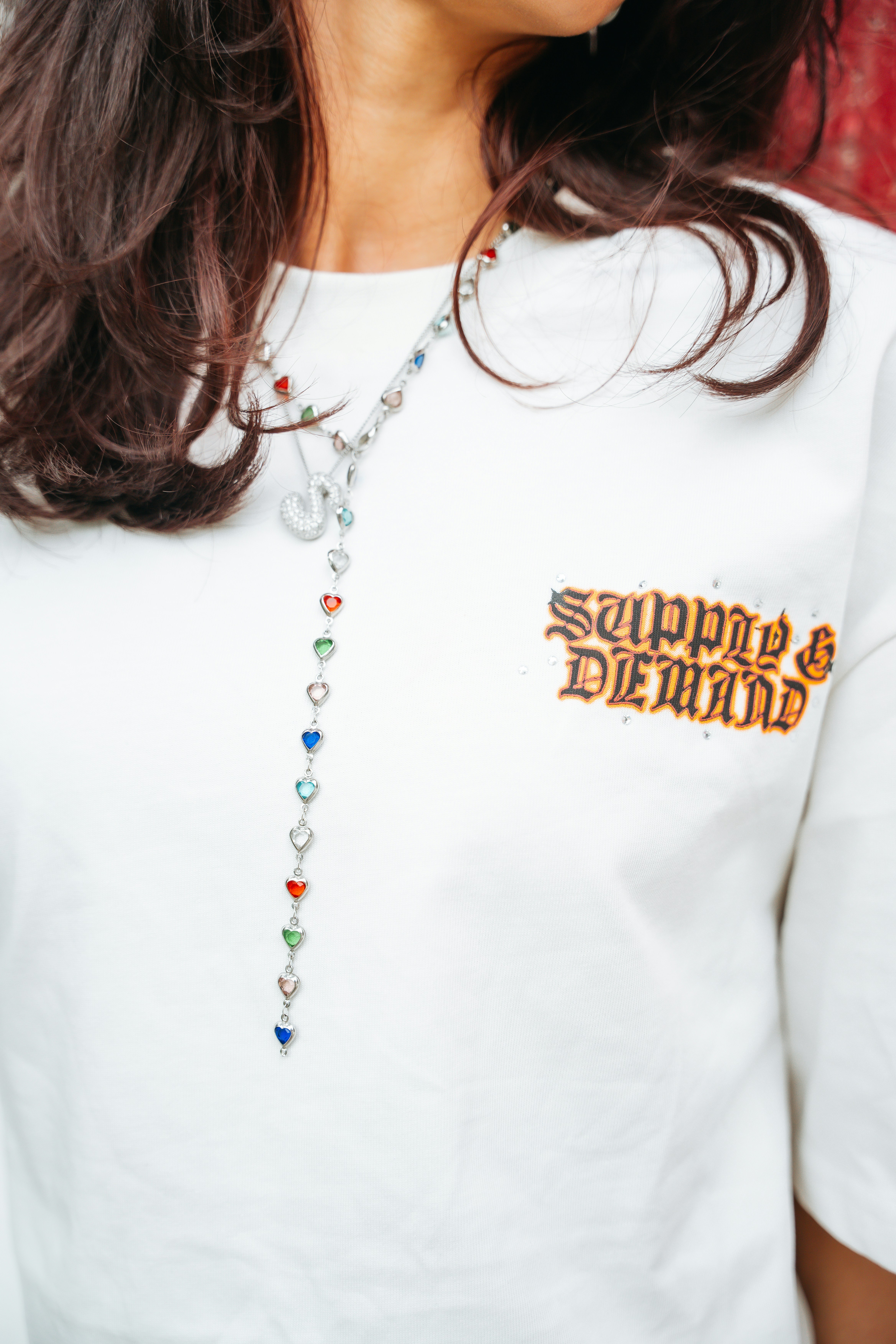 White t-shirt with "supply & demand" text and heart necklace