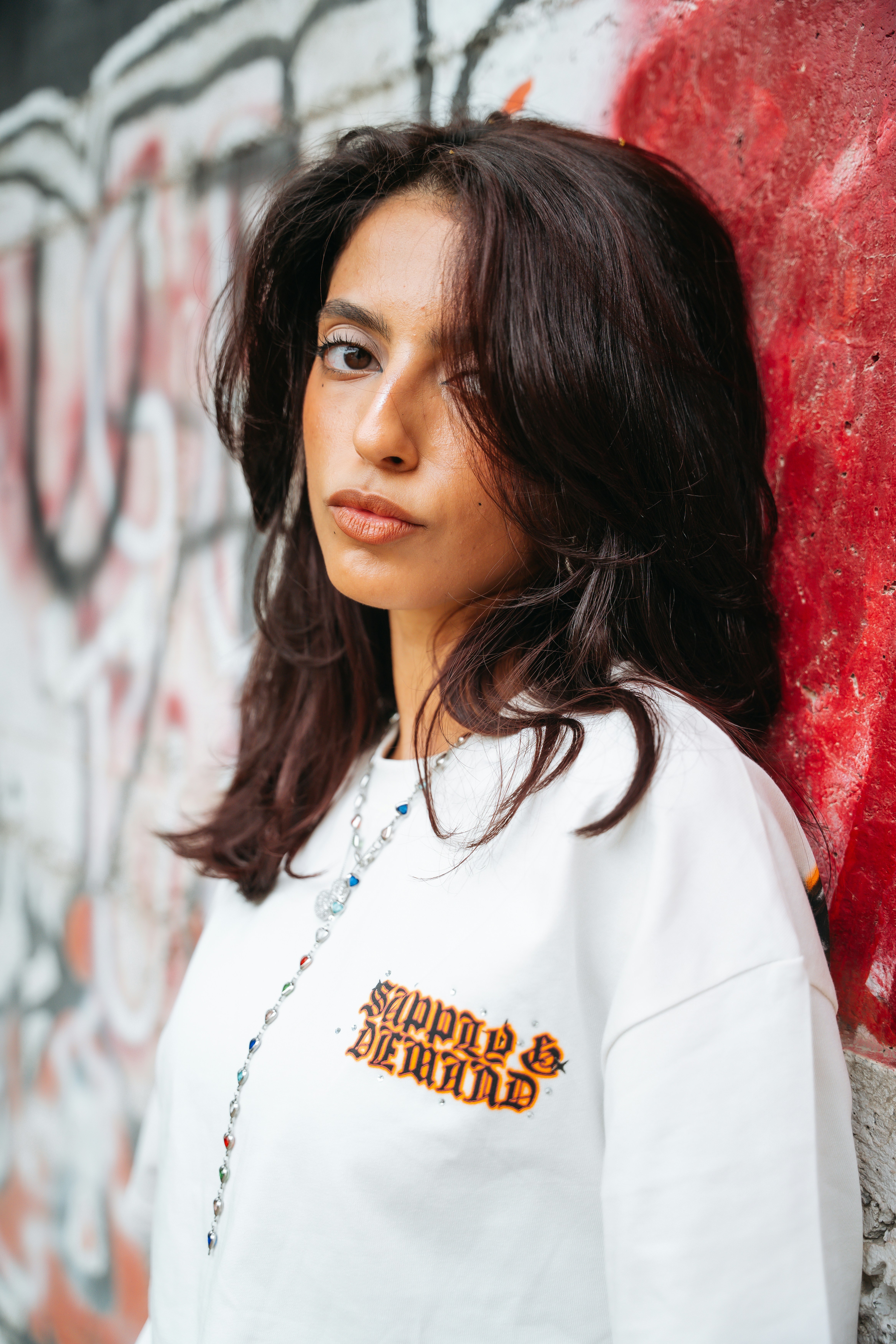 Young woman in white sweatshirt against a red graffiti wall.