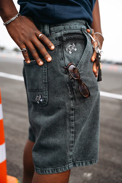 Person wearing dark denim shorts with sunglasses in pocket.