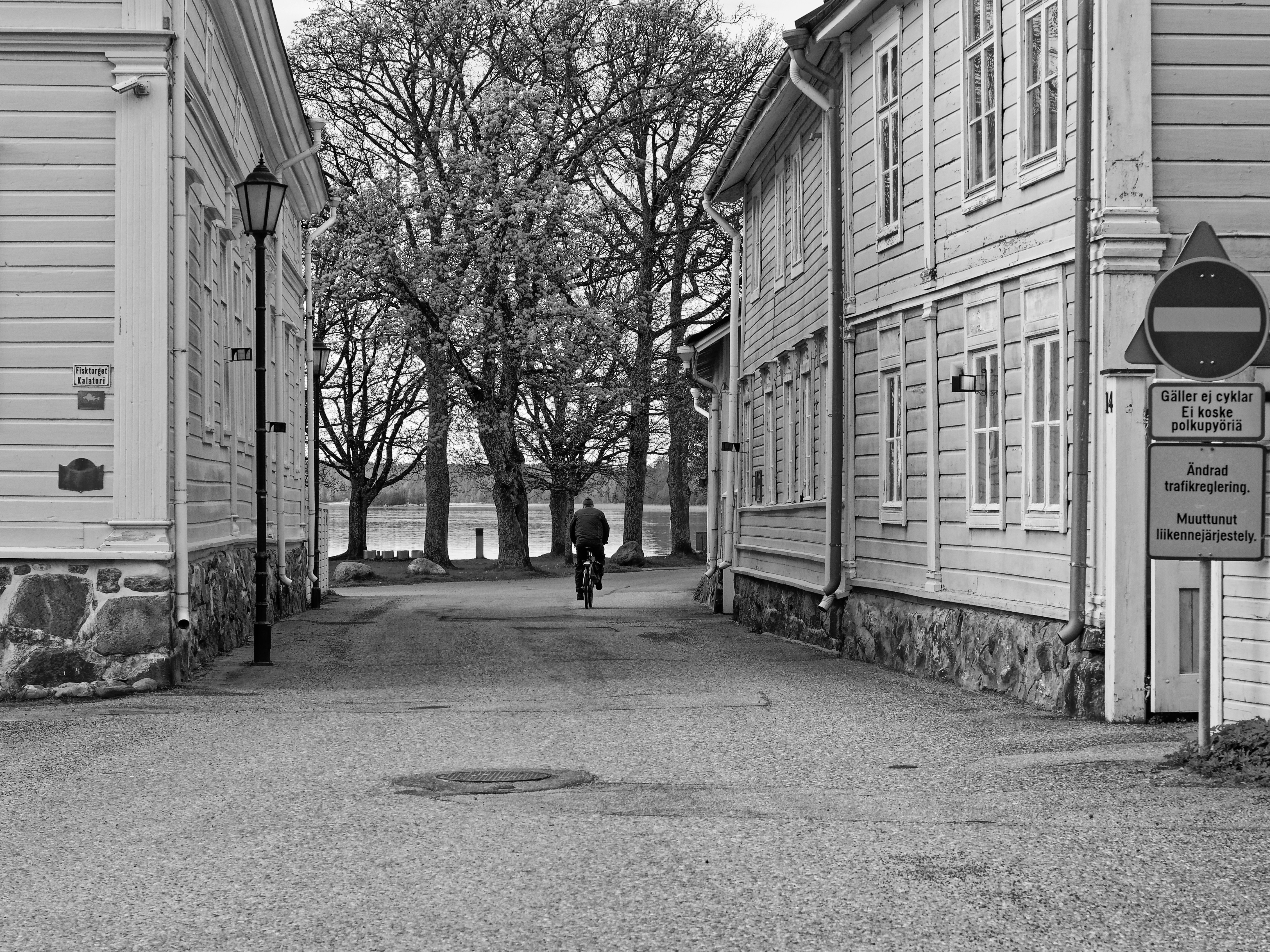 Person cycling between wooden buildings towards a lake