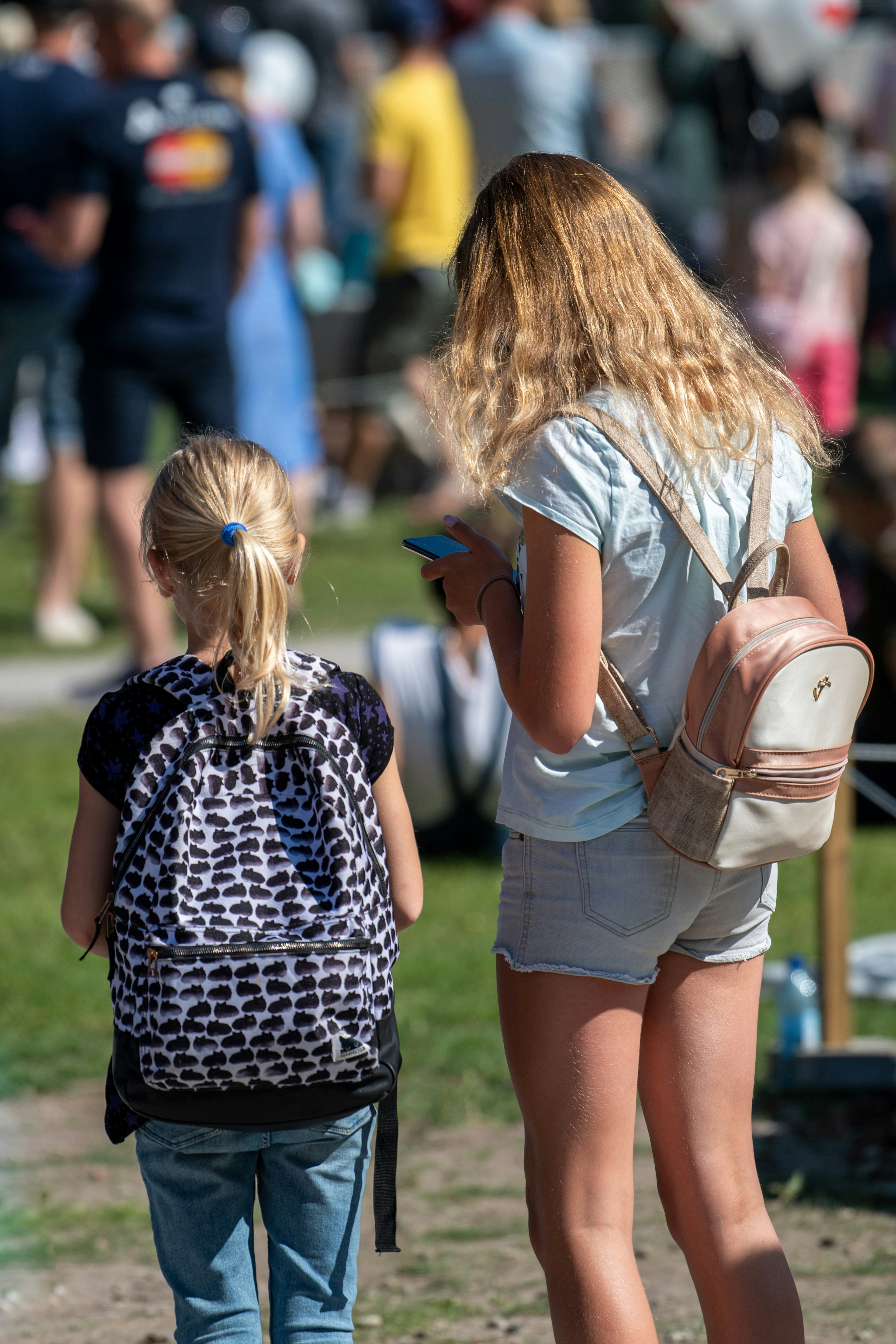 Two girls with backpacks in a crowd.