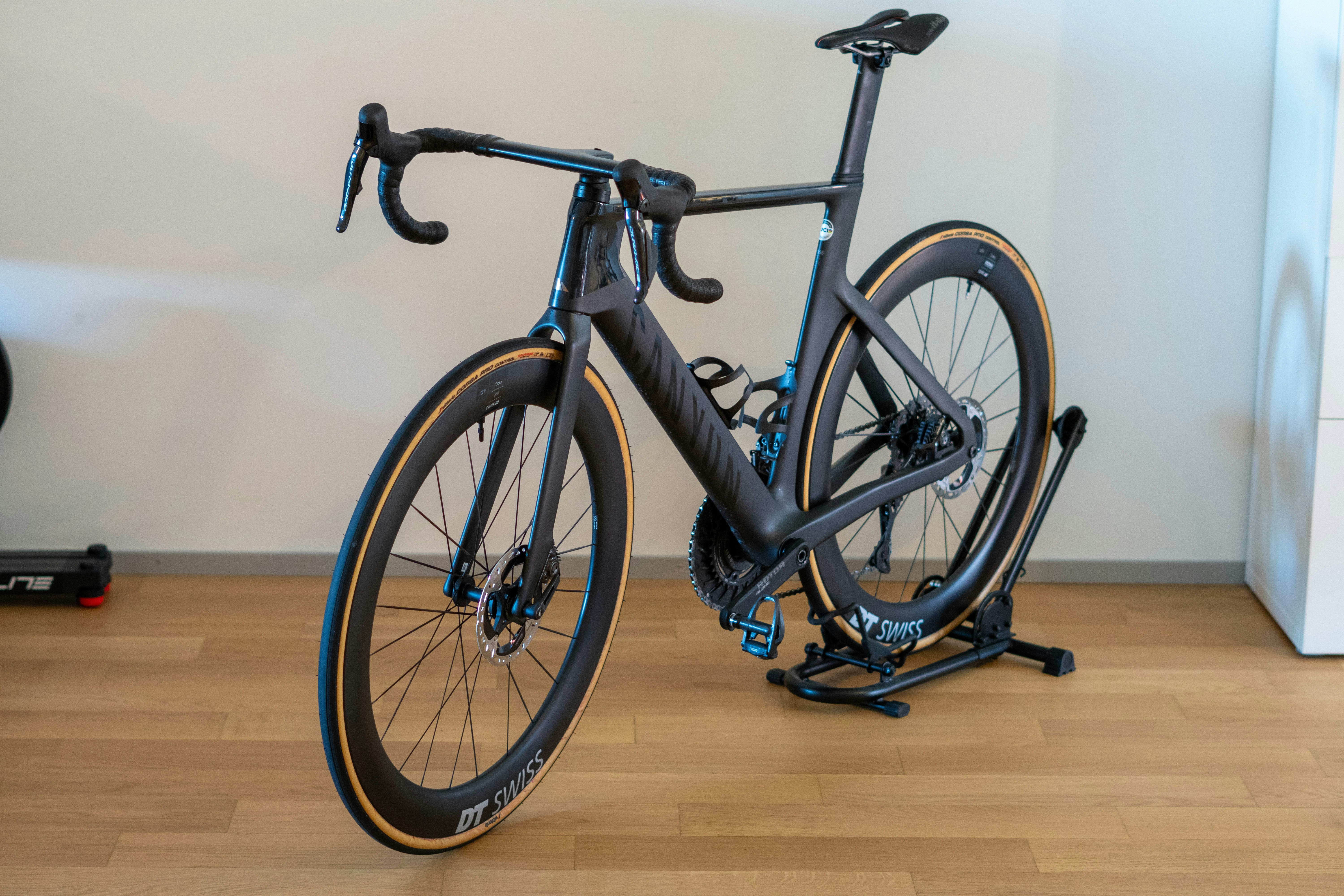 A black high-performance road bicycle on a stand indoors.