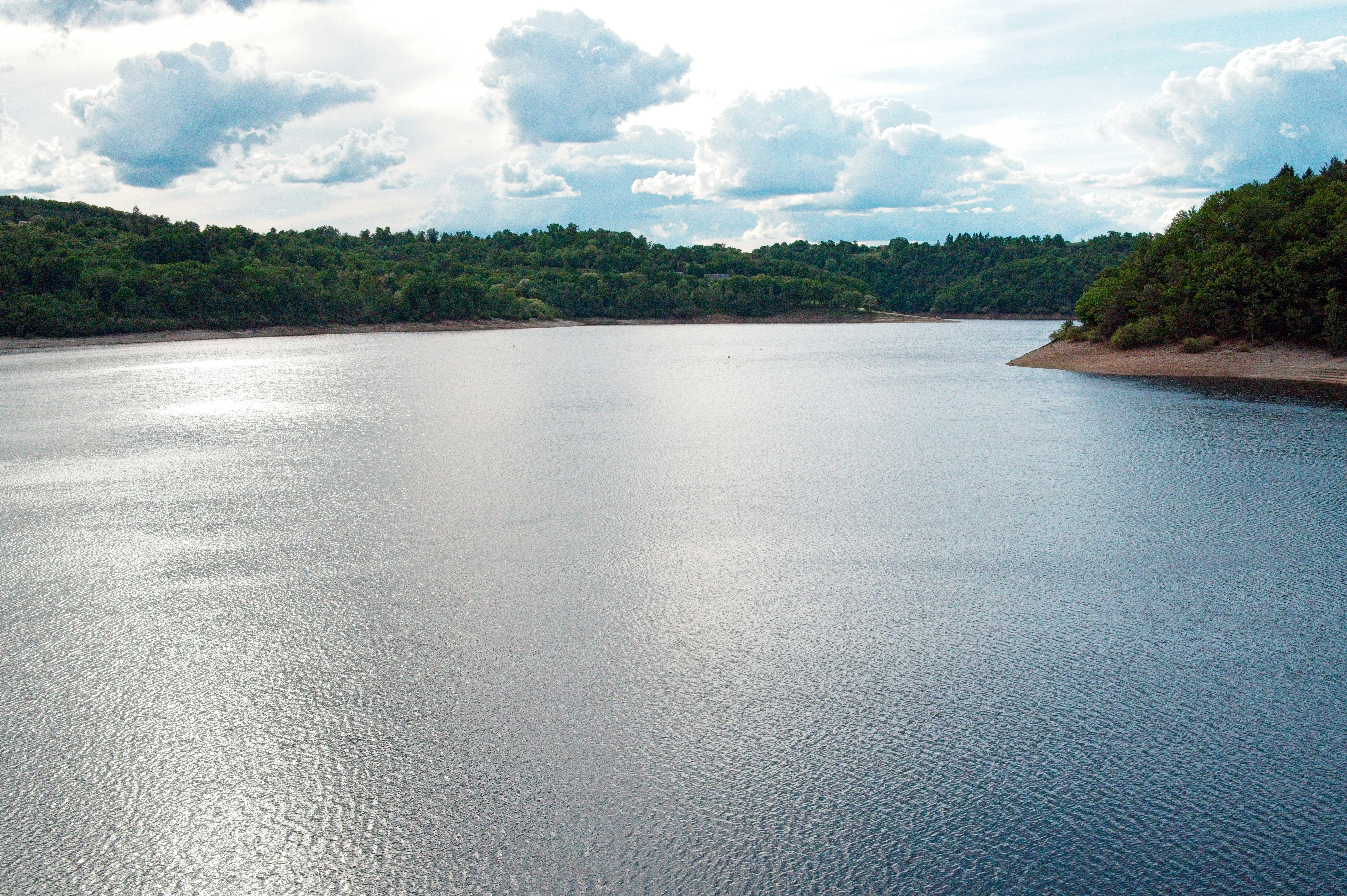 Danau tenang yang dikelilingi oleh pepohonan hijau di bawah langit mendung