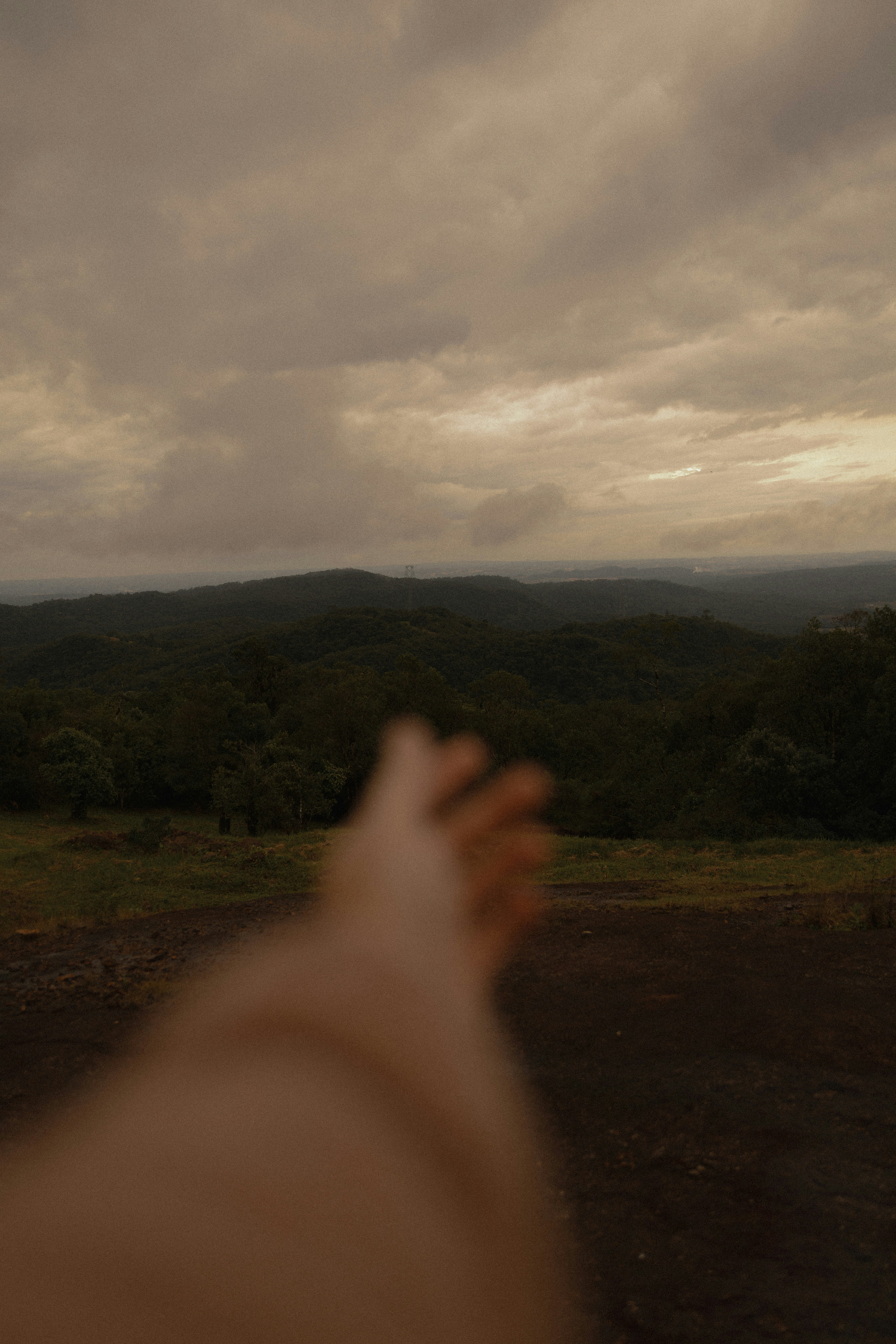 Hand reaching out towards rolling green hills under cloudy sky