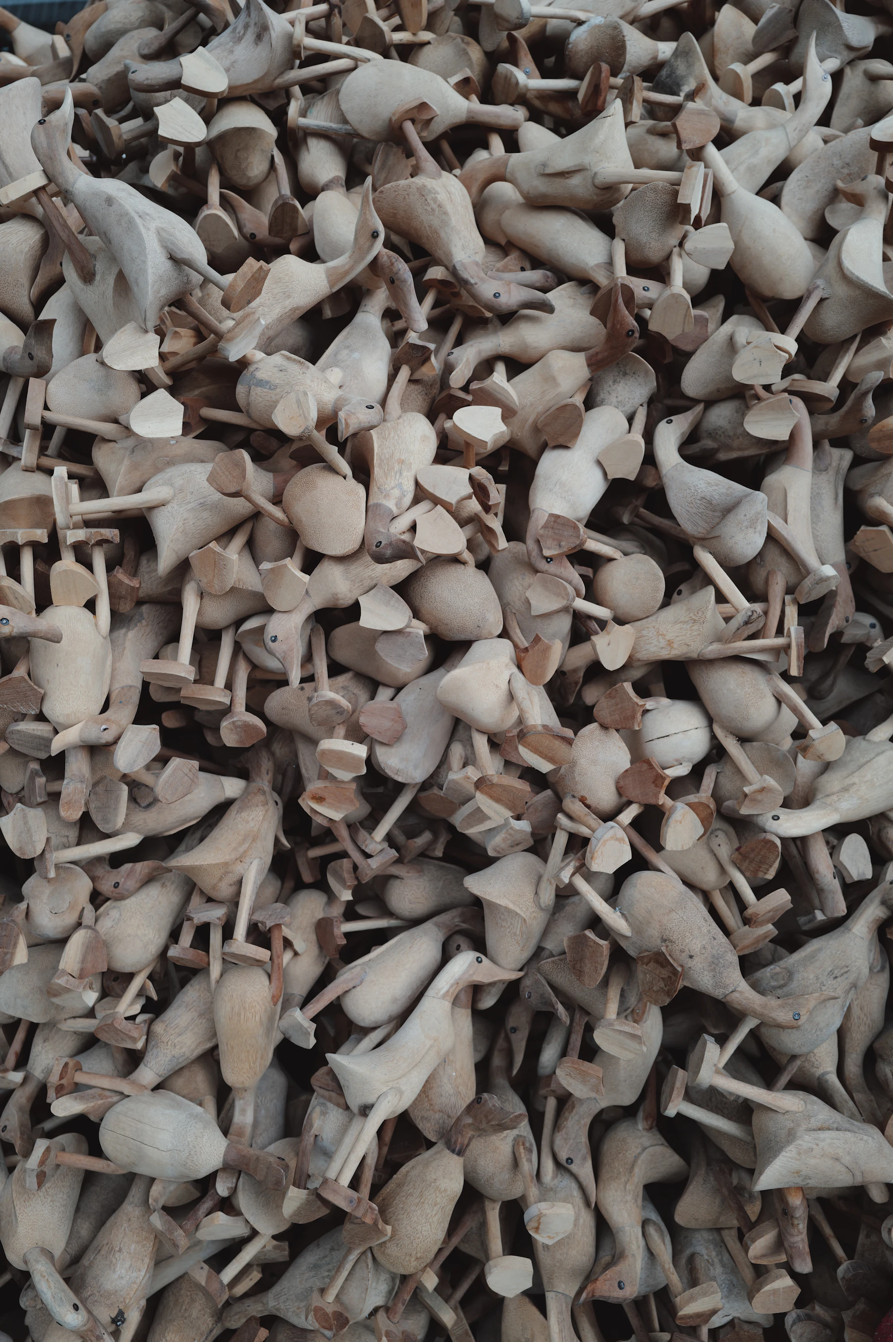 A deep pile of unfinished carved wooden ducks in bare wood, seen from above