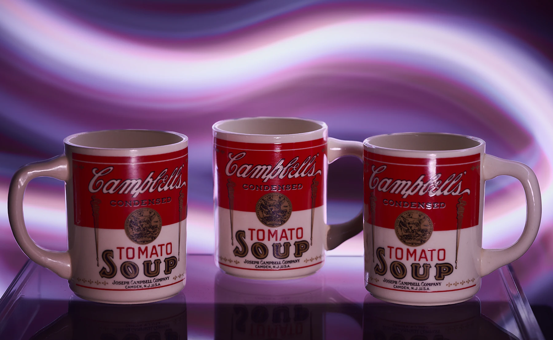 Three matching red and white advertising mugs printed like soup cans, standing on a glass shelf