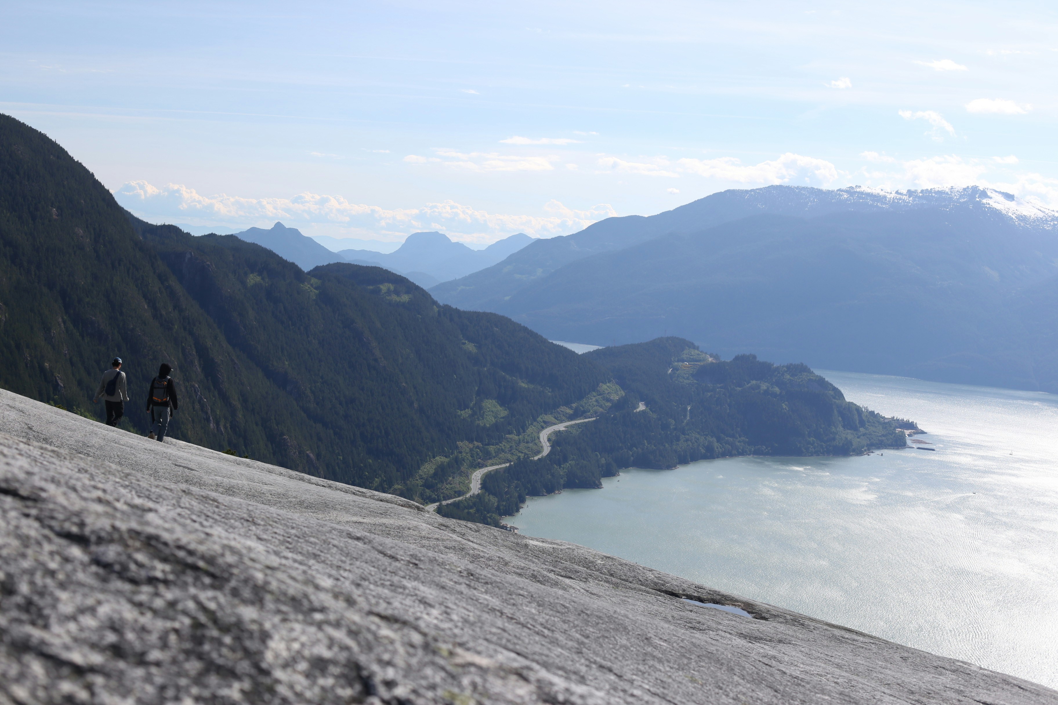 Wanderer auf einem steilen Felsen mit Blick auf einen Bergsee.