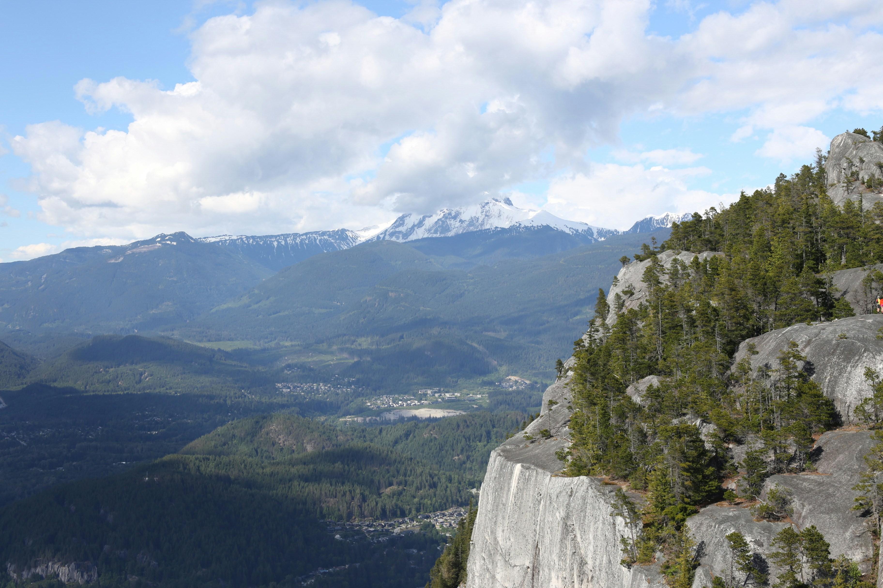 Schneebedeckte Berge mit Blick auf ein bewaldetes Tal und eine Felswand.
