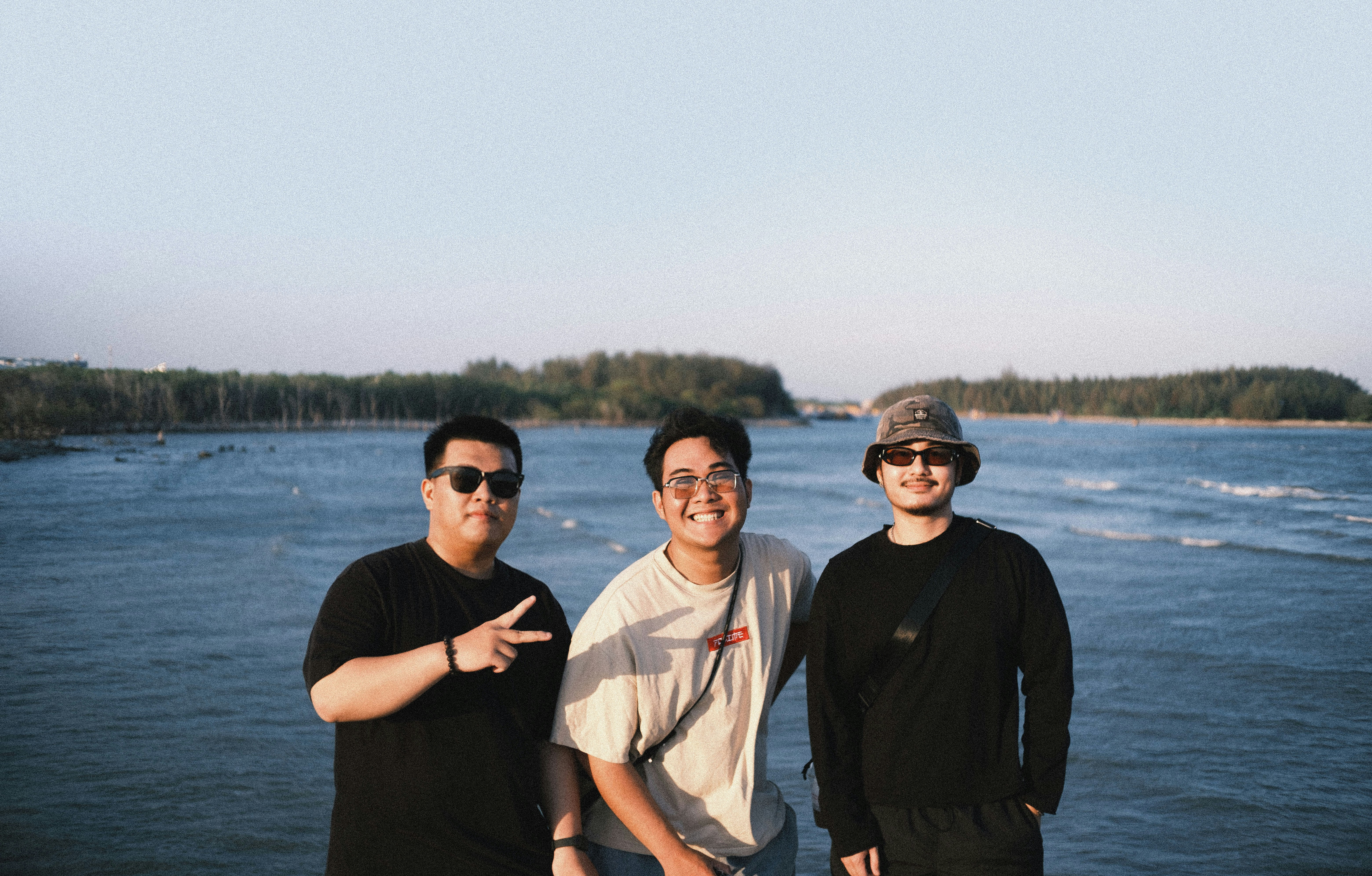 Tiga pria tersenyum di depan lautan.