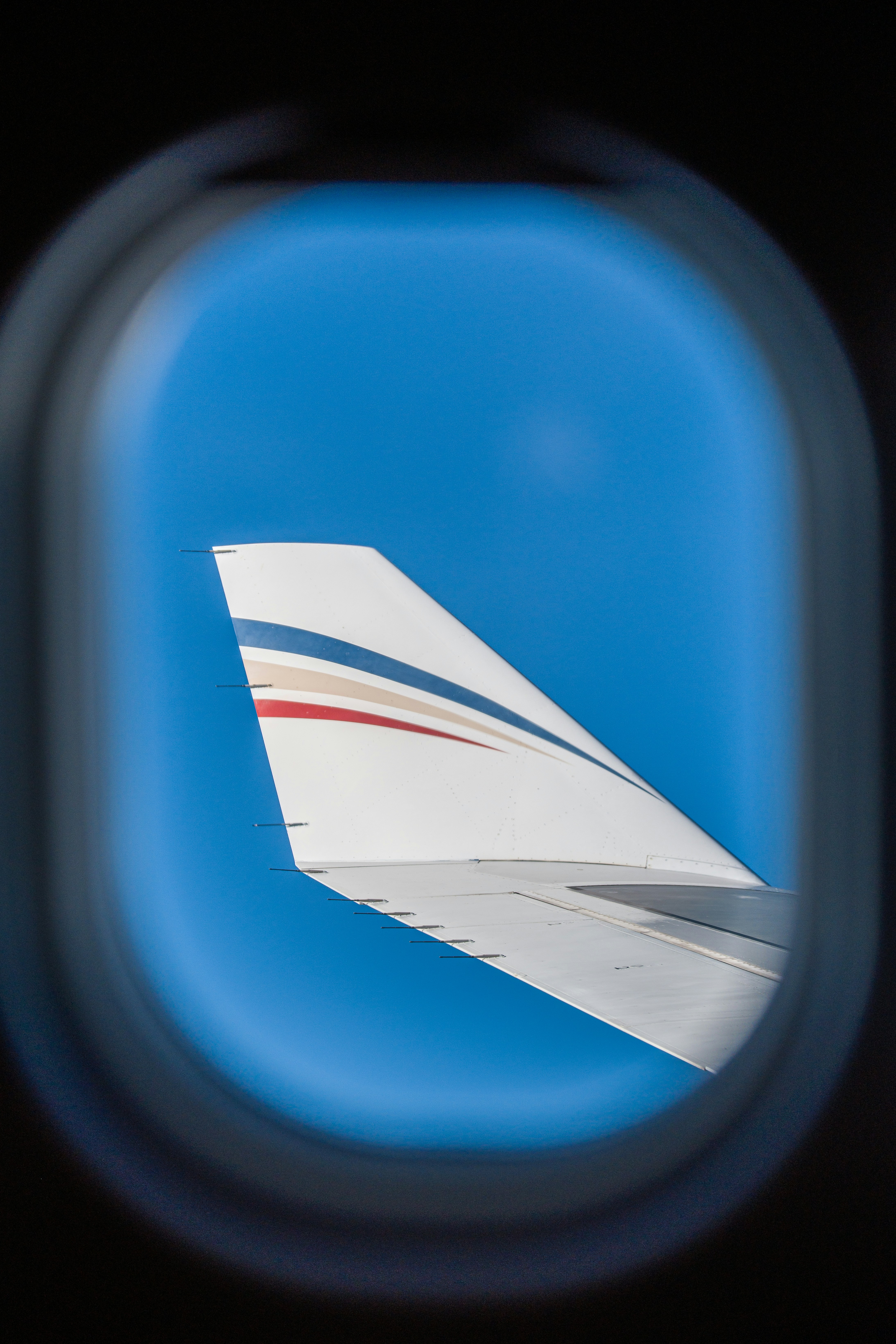 Flugzeugflügel sichtbar durch ein Bullauge gegen den blauen Himmel.