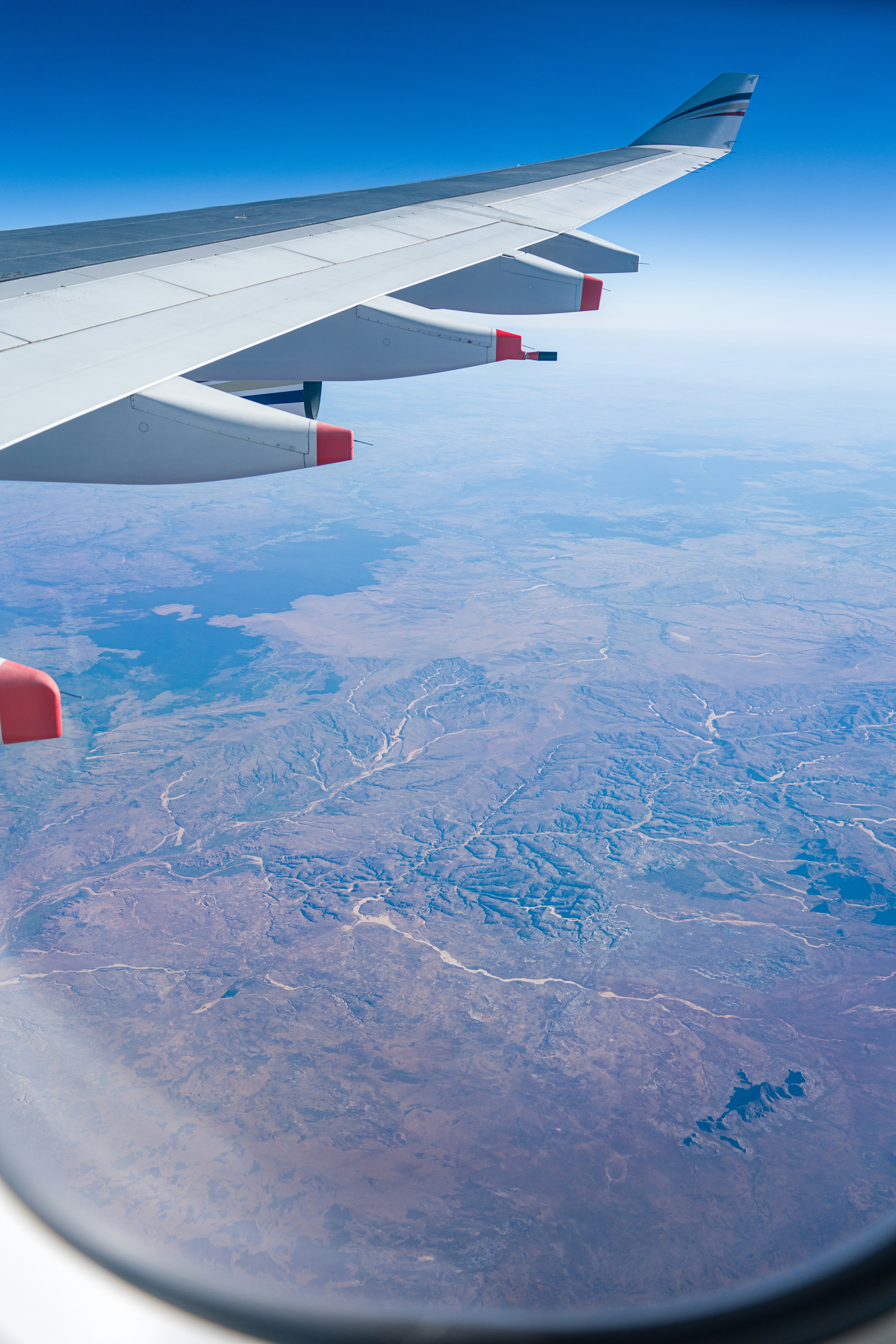Flugzeugflügel schwebt über einer trockenen, zerklüfteten Landschaft.