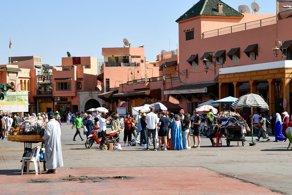 Place Jemaa el-Fna animée, avec ses vendeurs et ses bâtiments ocre rose, à Marrakech