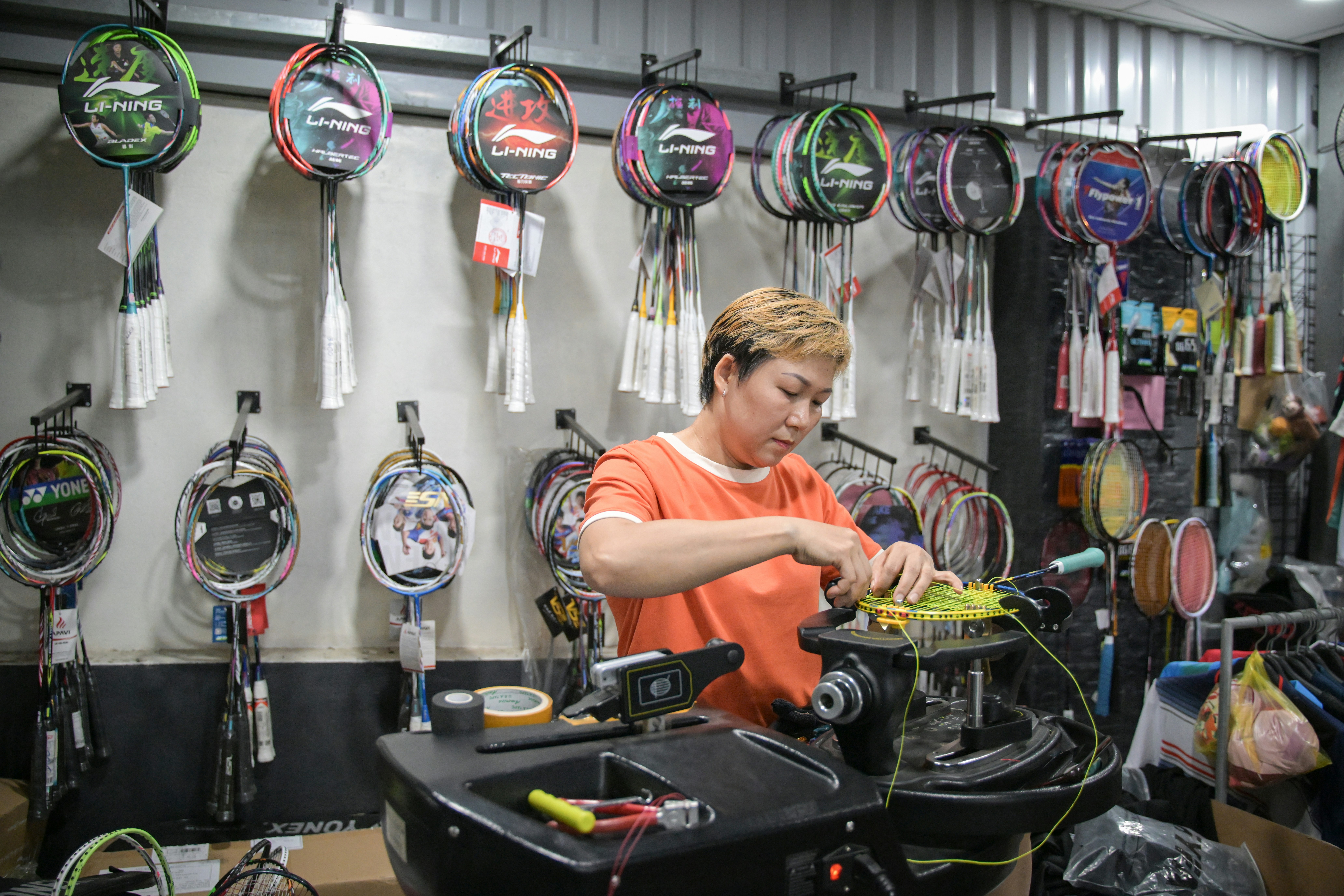 A woman strings a badminton racket in a sports shop.