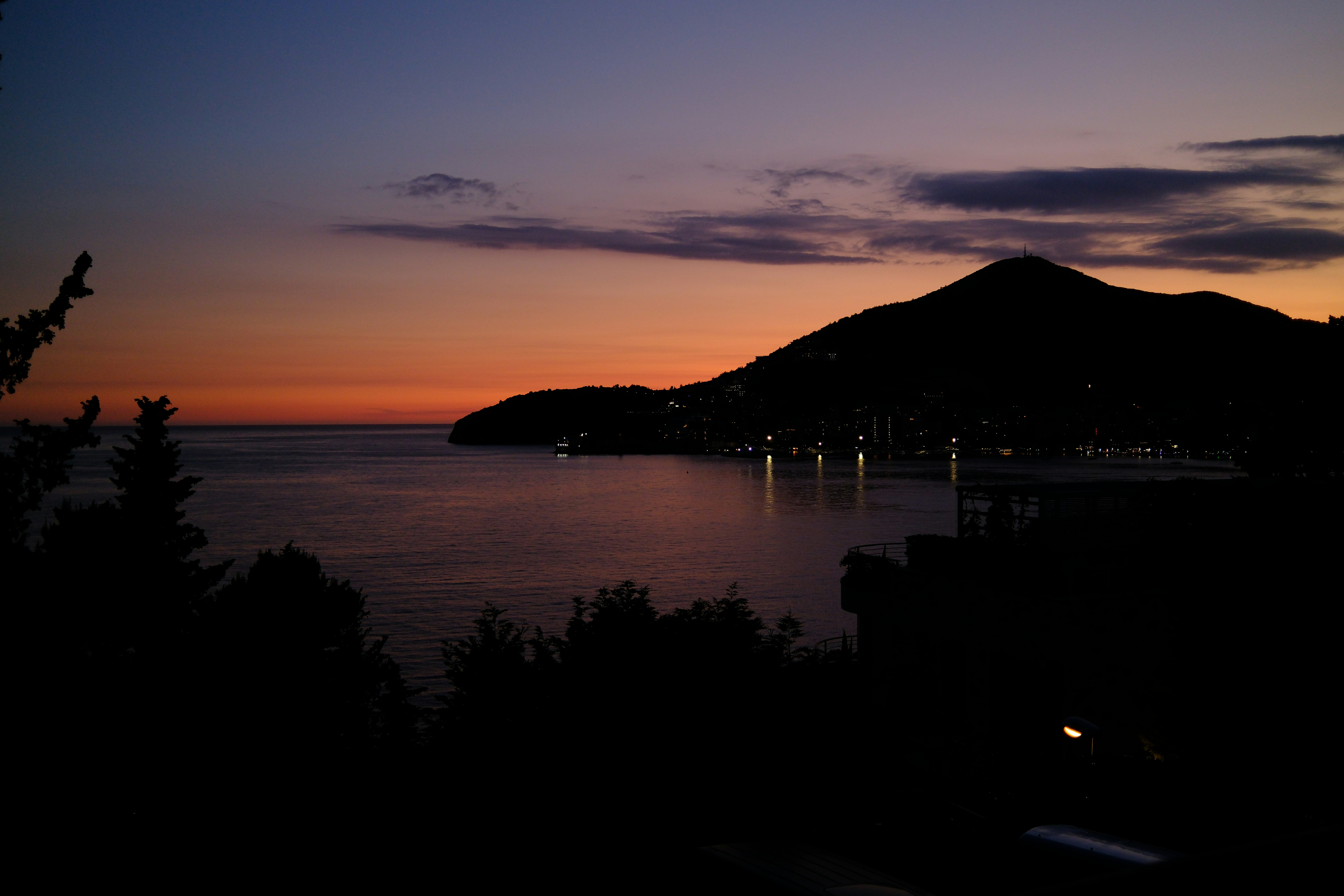 Un coucher de soleil vibrant sur une ville côtière et des montagnes sombres.
