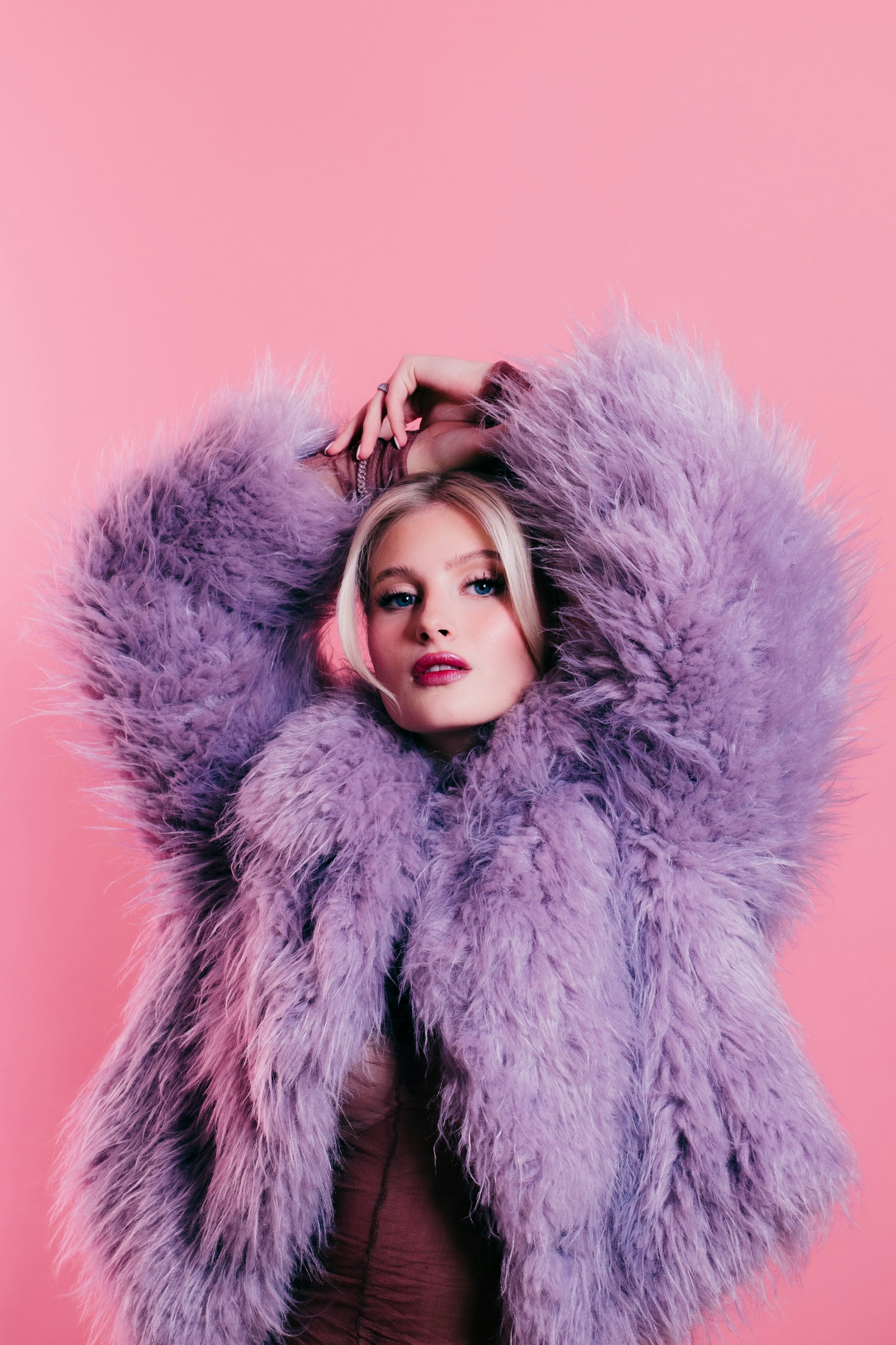 Mulher com casaco de pelo sintético lilás e rosa em editorial colorido