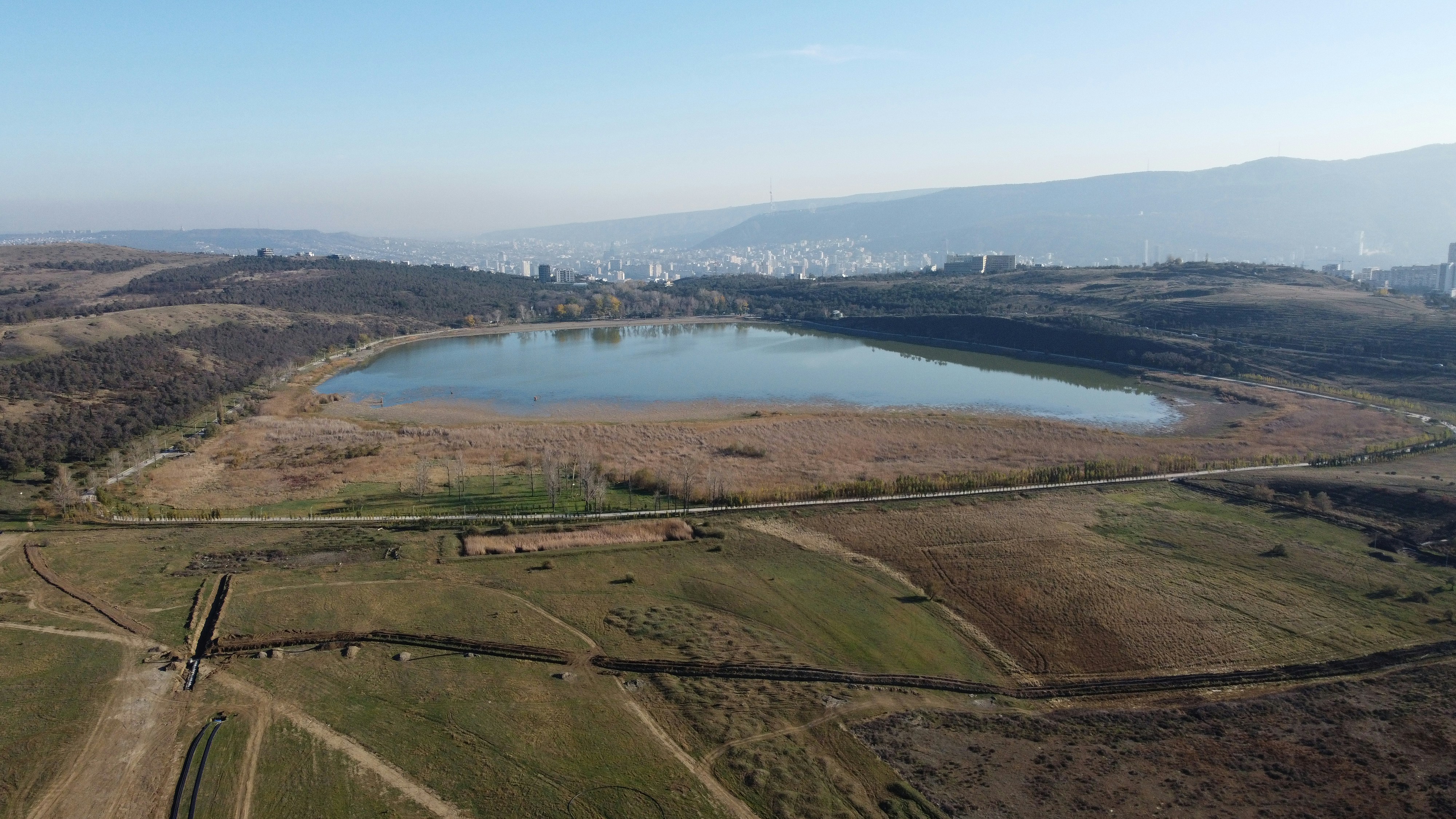 Expansive lake in dry fields with distant city skyline.