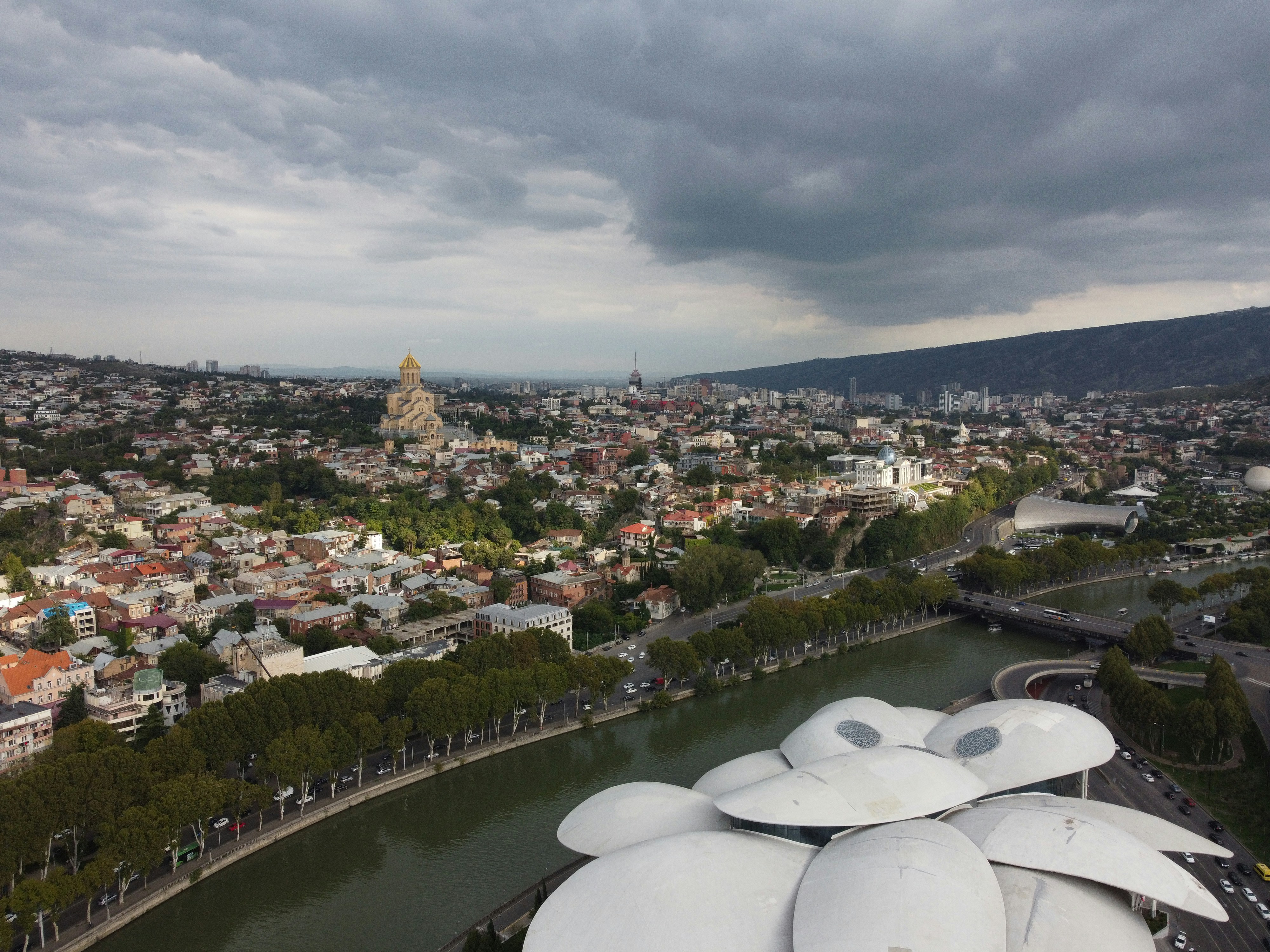 City panorama with a river, modern architecture, and cloudy sky.