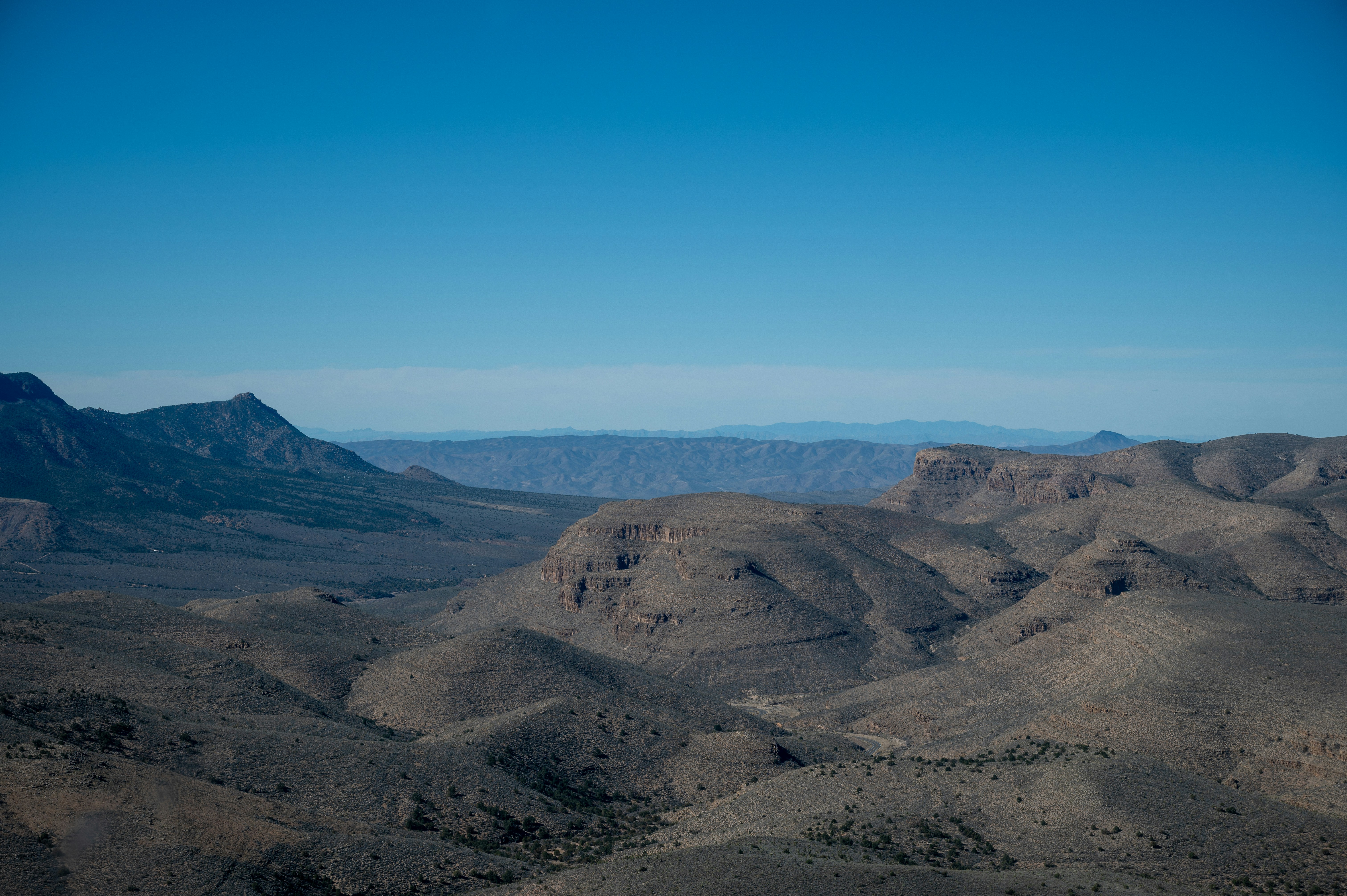 Vast desert landscape with mountains and hills under blue sky.