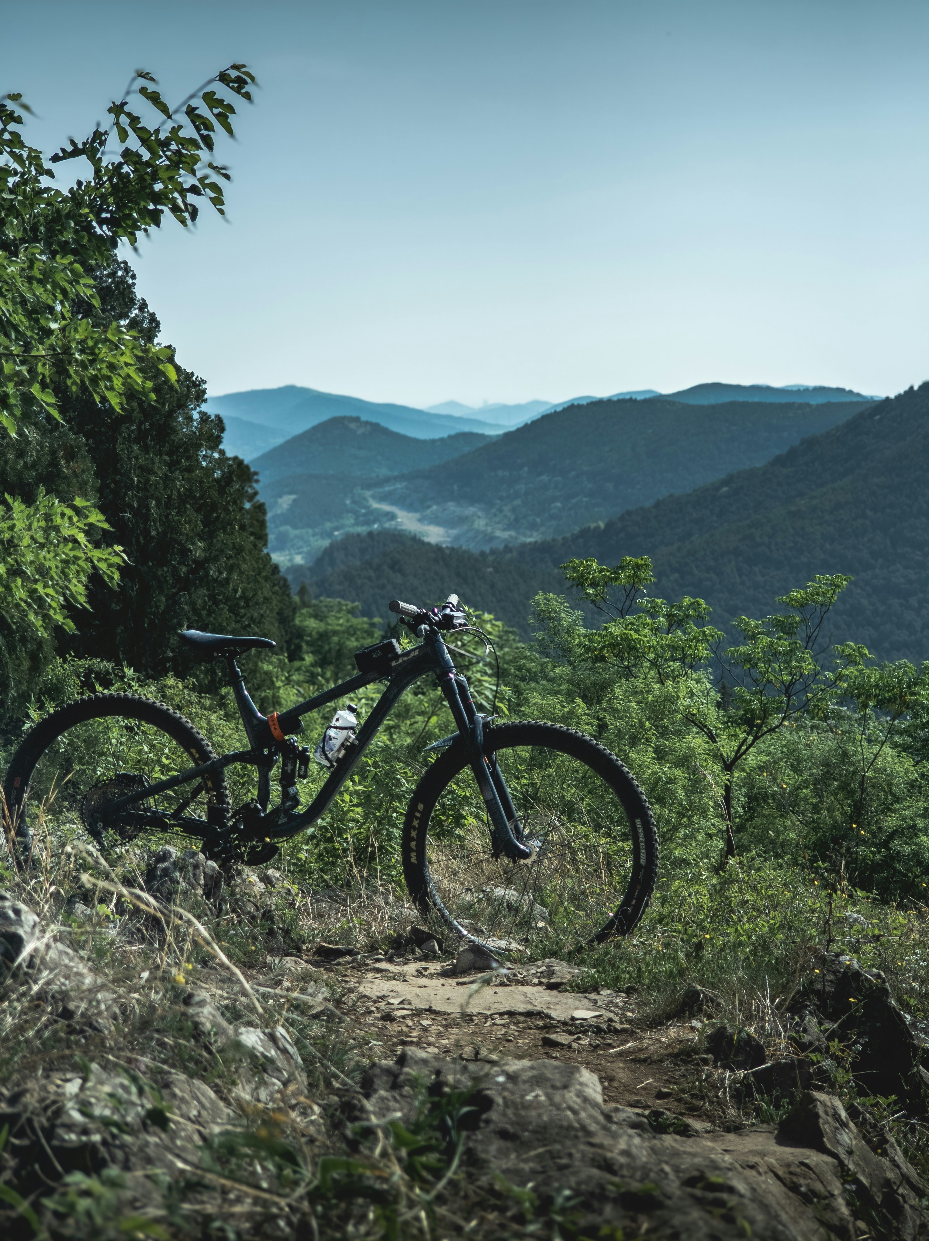 A mountain bike rests on a trail overlooking scenic hills.
