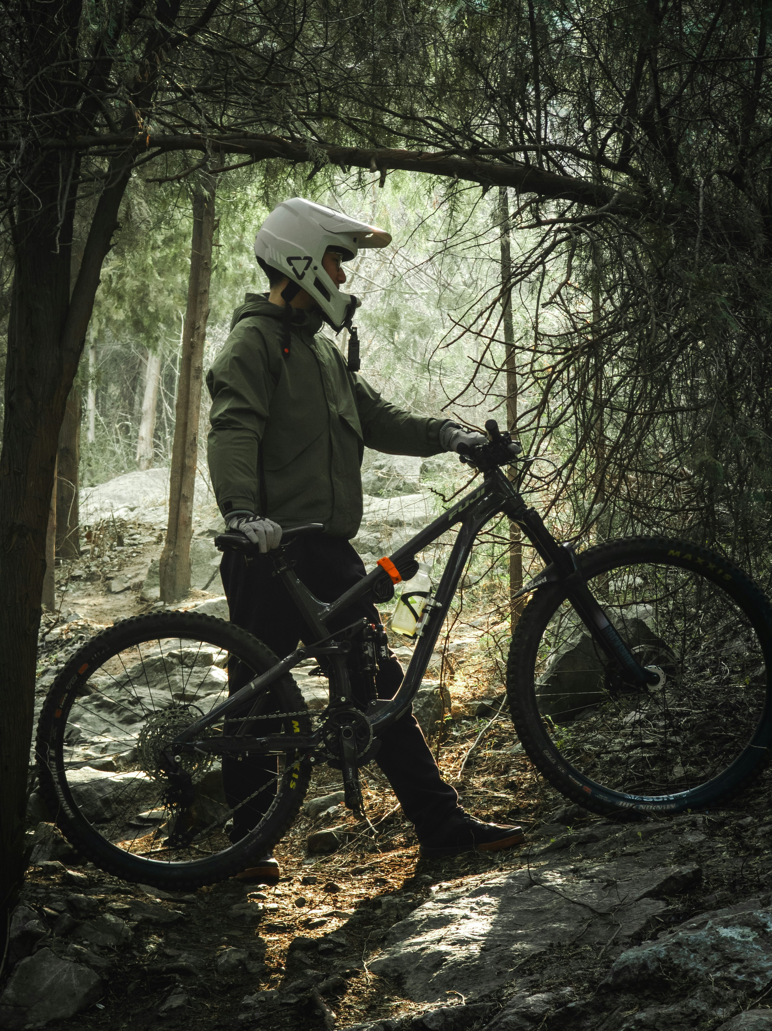 Biker in helmet stands with mountain bike in forest.