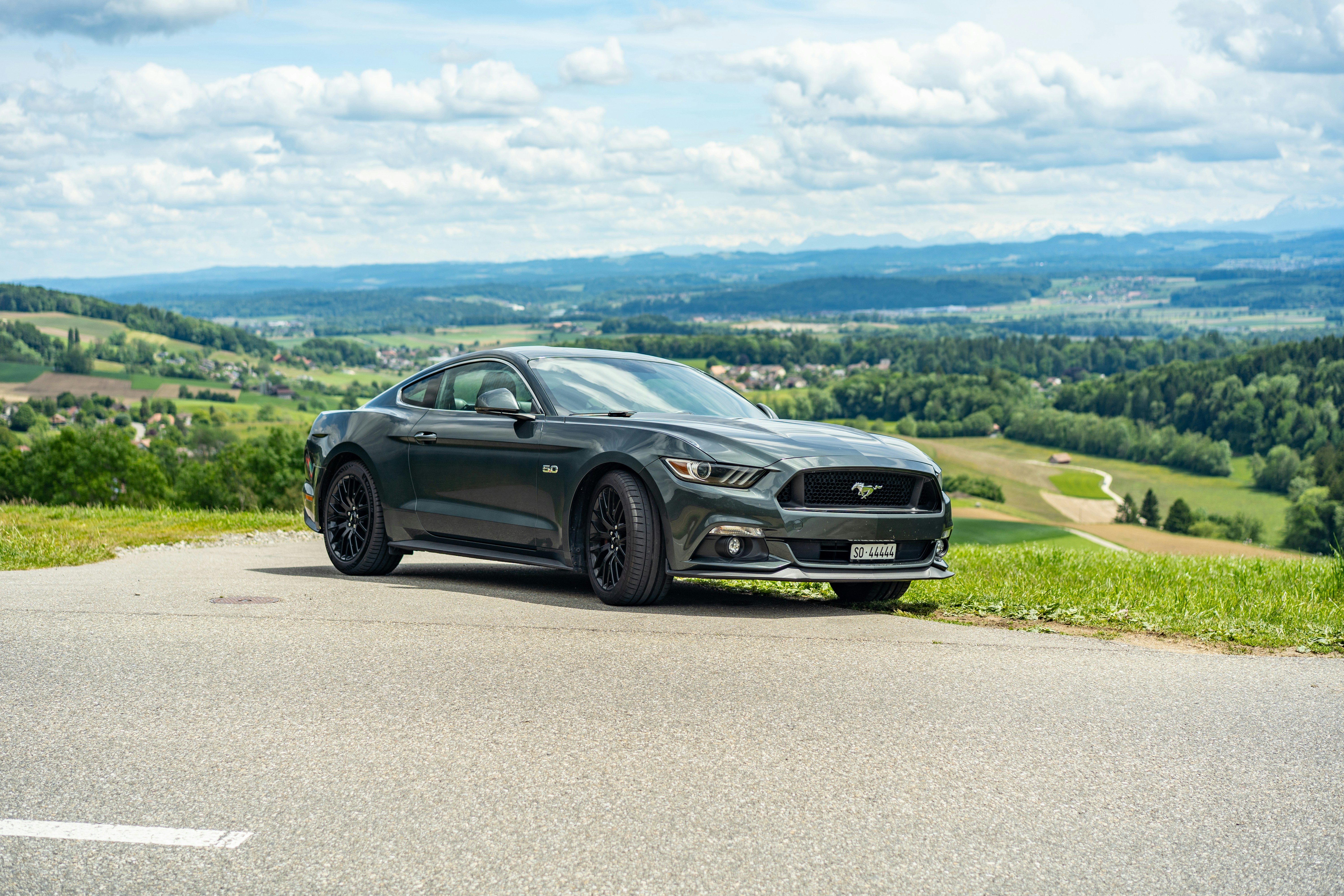 Une Ford Mustang gris foncé garée sur une route pittoresque.