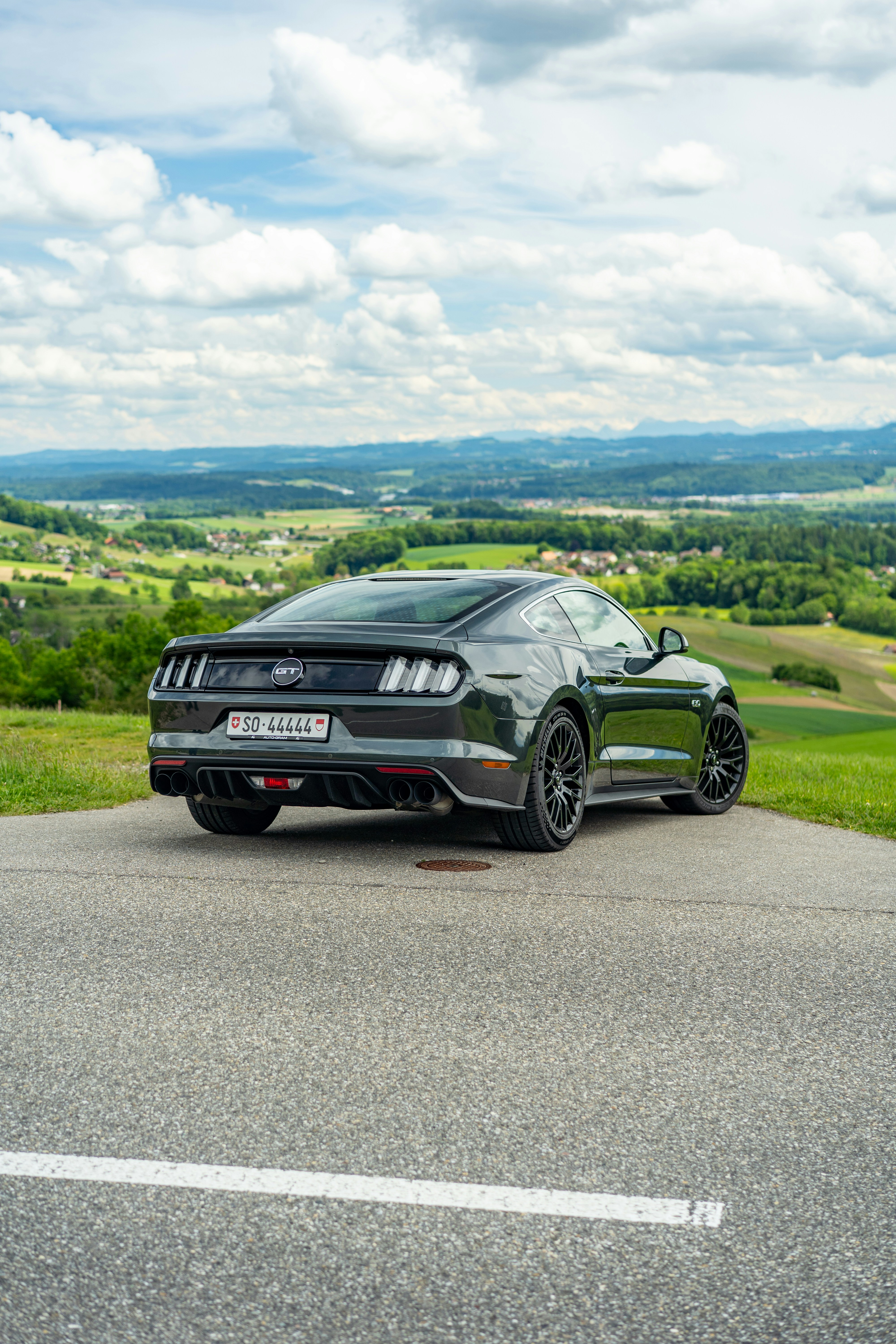 Une Ford Mustang gris foncé était garée surplombant des collines vertes.