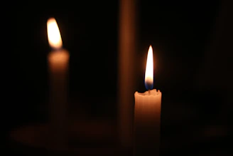 Two lit candles glow warmly in a dark room.