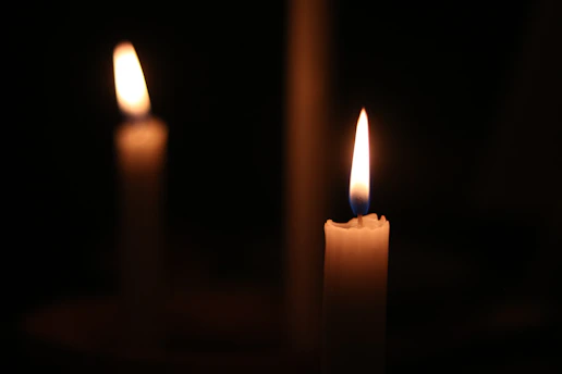 Two lit candles glow warmly in a dark room.