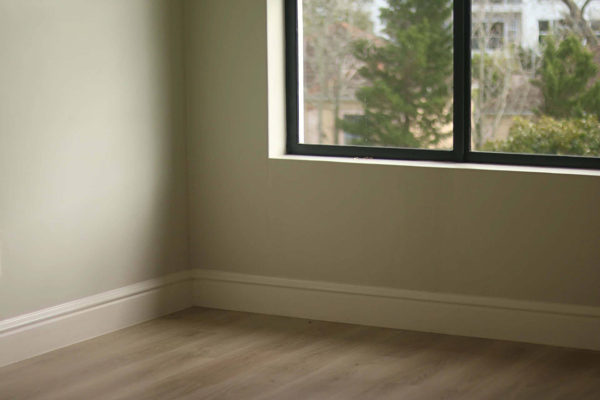 Empty room with light green walls, wooden floor, and window.