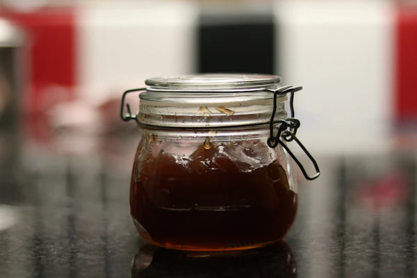 An unlabelled clip-top glass jar of dark jam on a reflective countertop