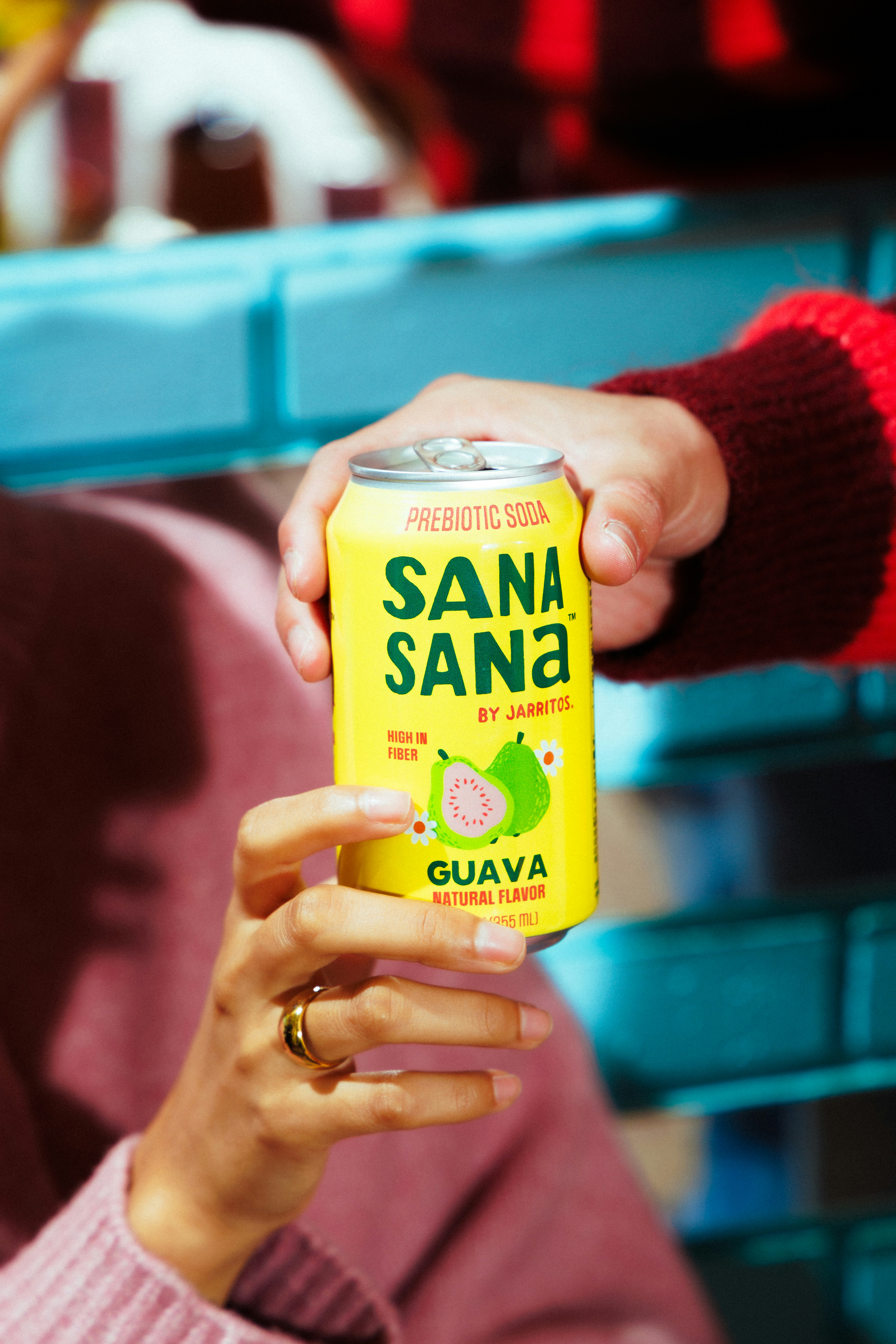 Dos manos sosteniendo una lata amarilla de refresco sana sana guayaba.