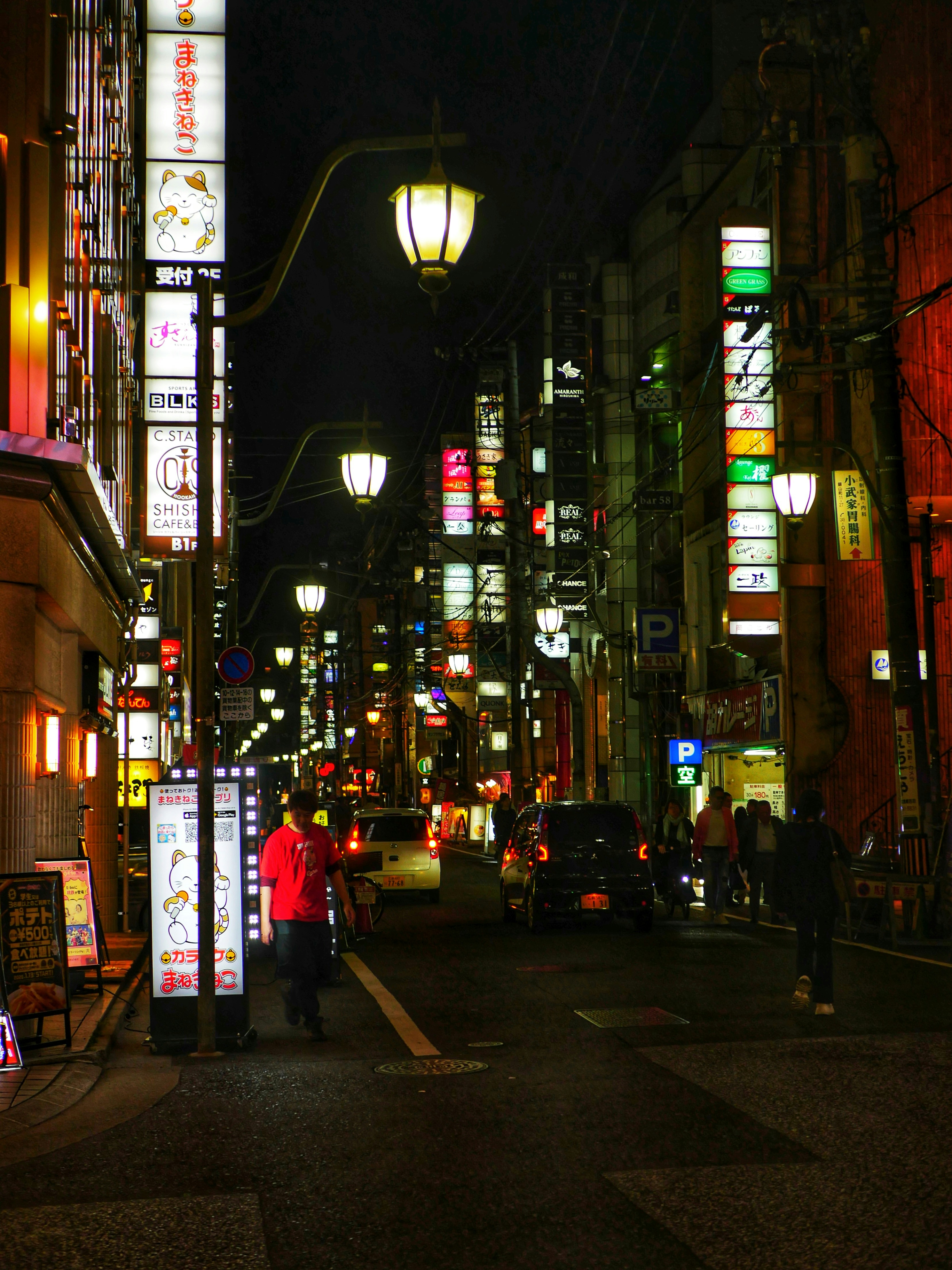 Calle urbana de noche iluminada por carteles coloridos y farolas.