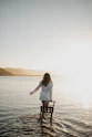 Woman in white shirt walks in water with chair.