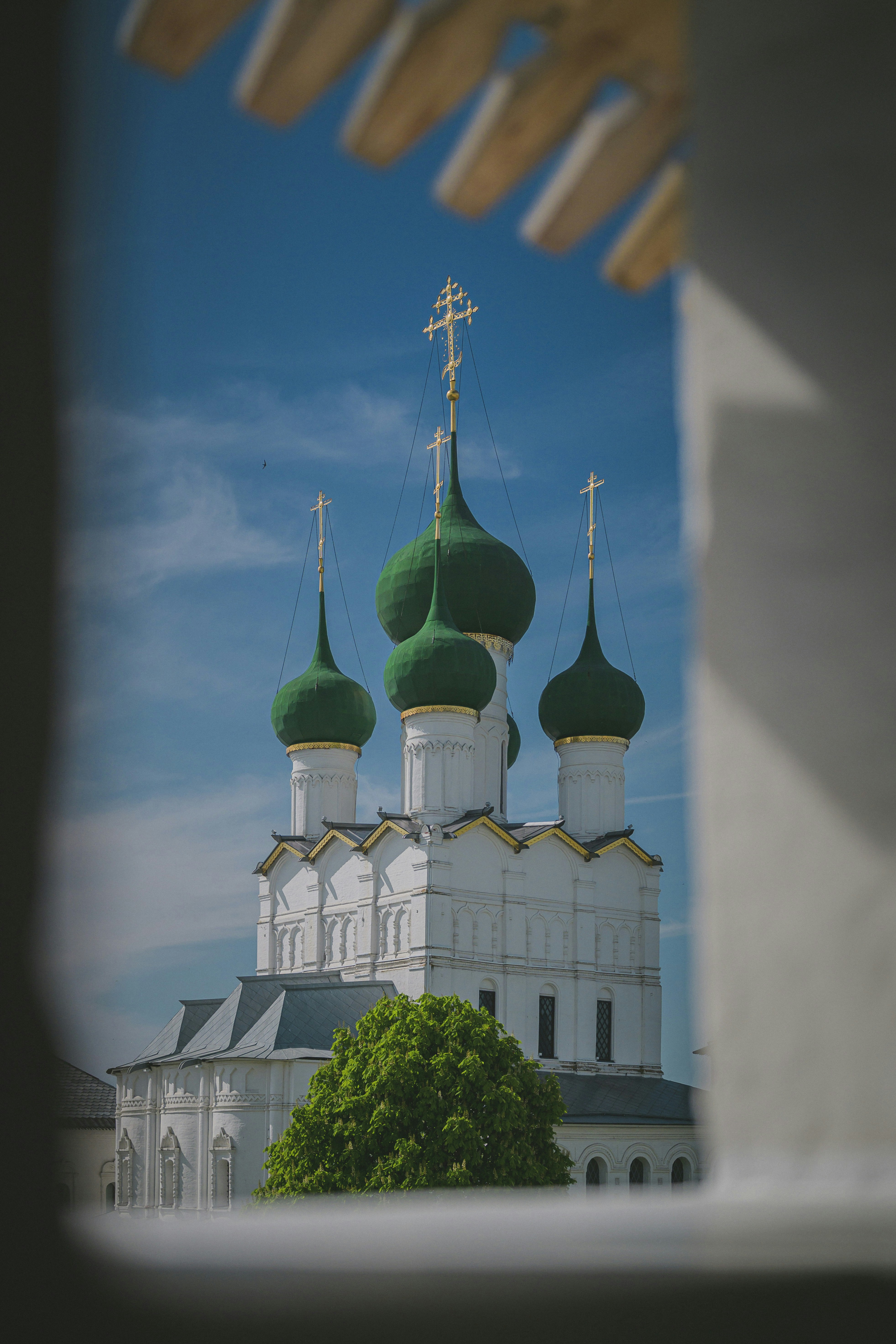 White church with green domes framed against a blue sky.