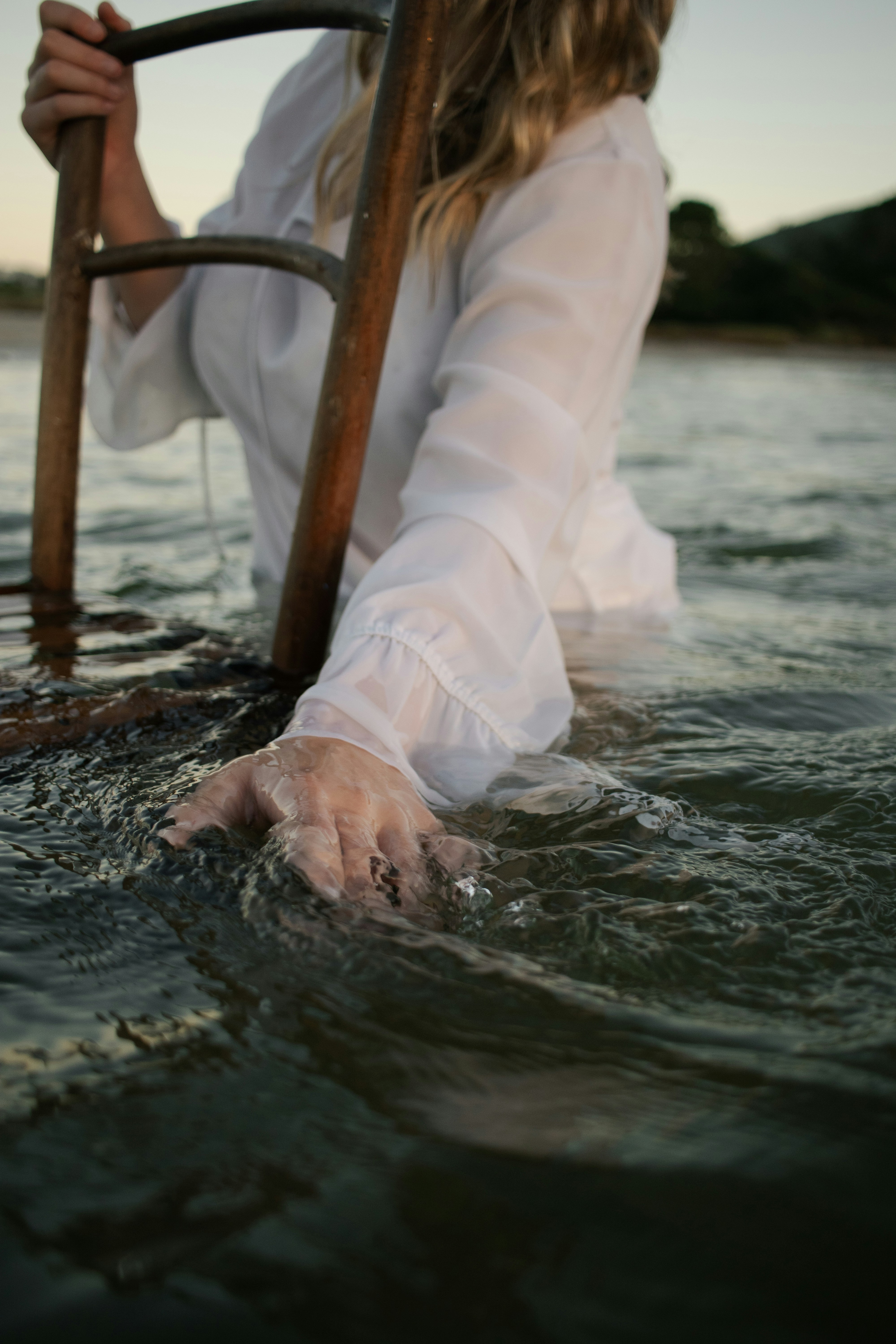 Woman in white shirt holding a wooden ladder in water.