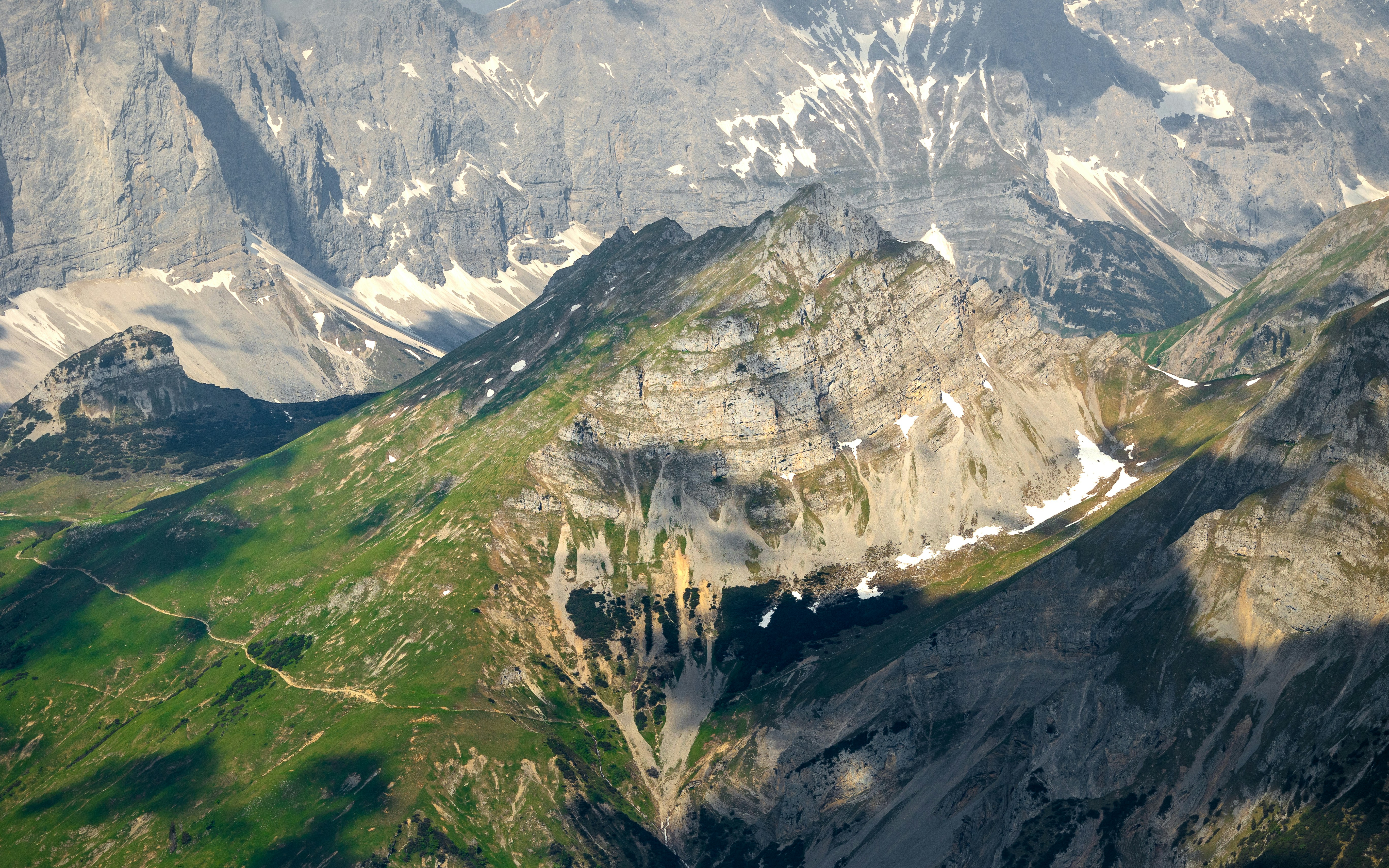 Montagne aspre con pendii verdi e cime innevate.