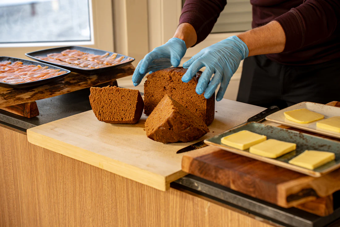 Hands in gloves finishing a plate of dark bread, cured meat and butter