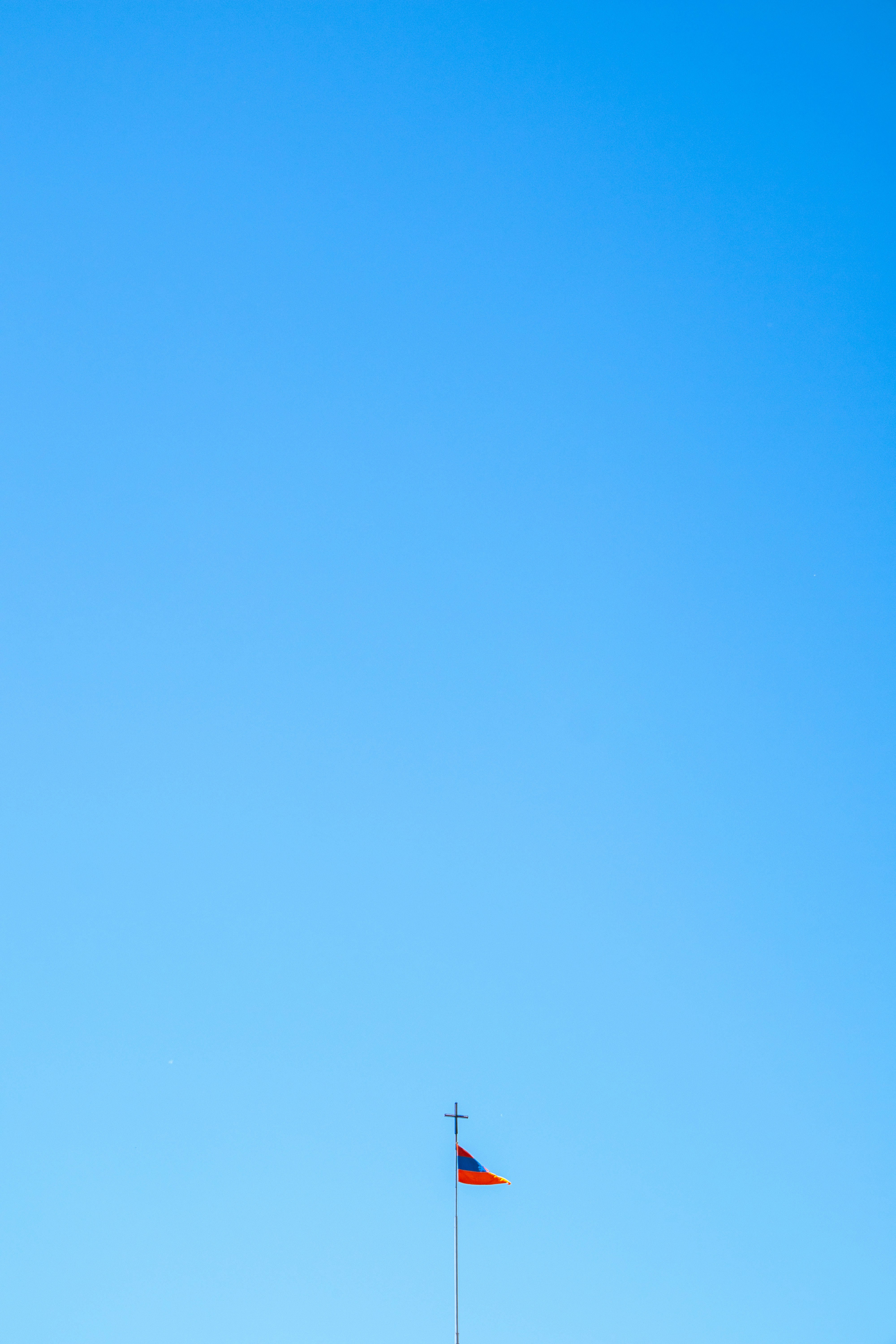 Kleine Fahne mit einem Kreuz vor klarem blauen Himmel.